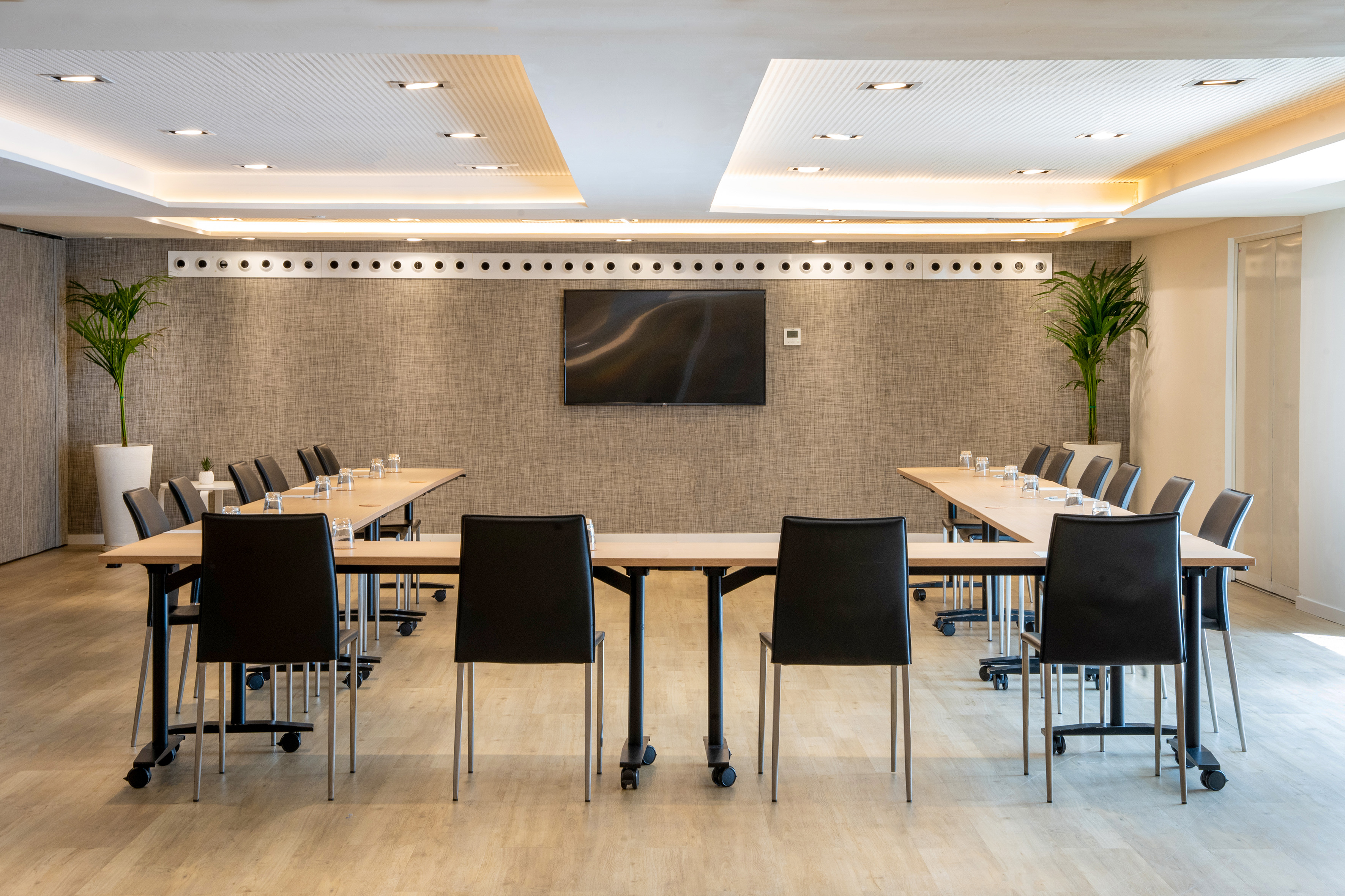 Modern meeting room with U-shaped table, black chairs, TV, and recessed lighting.