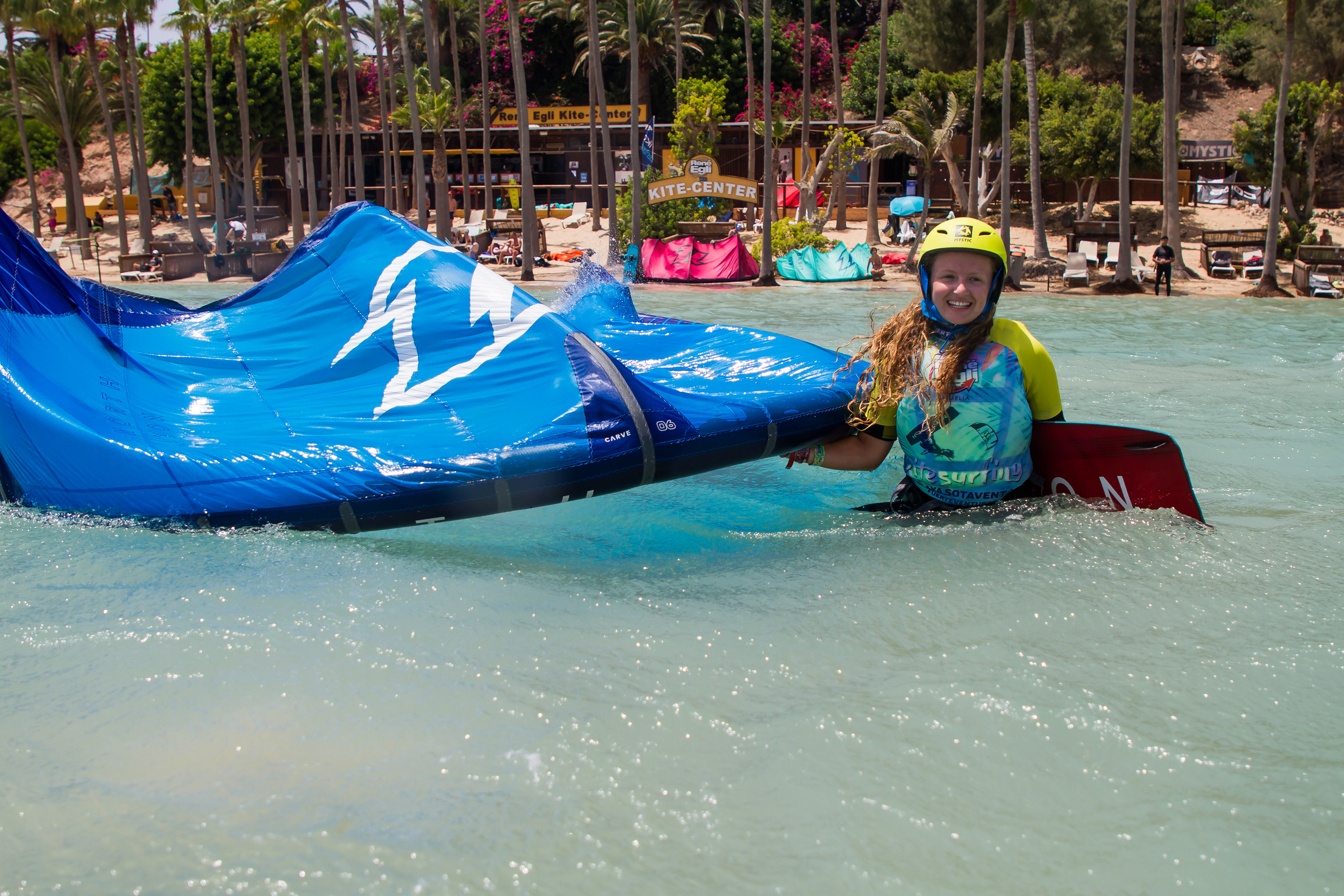 Kitesurfer in yellow helmet holding blue kite in tropical shallow water.