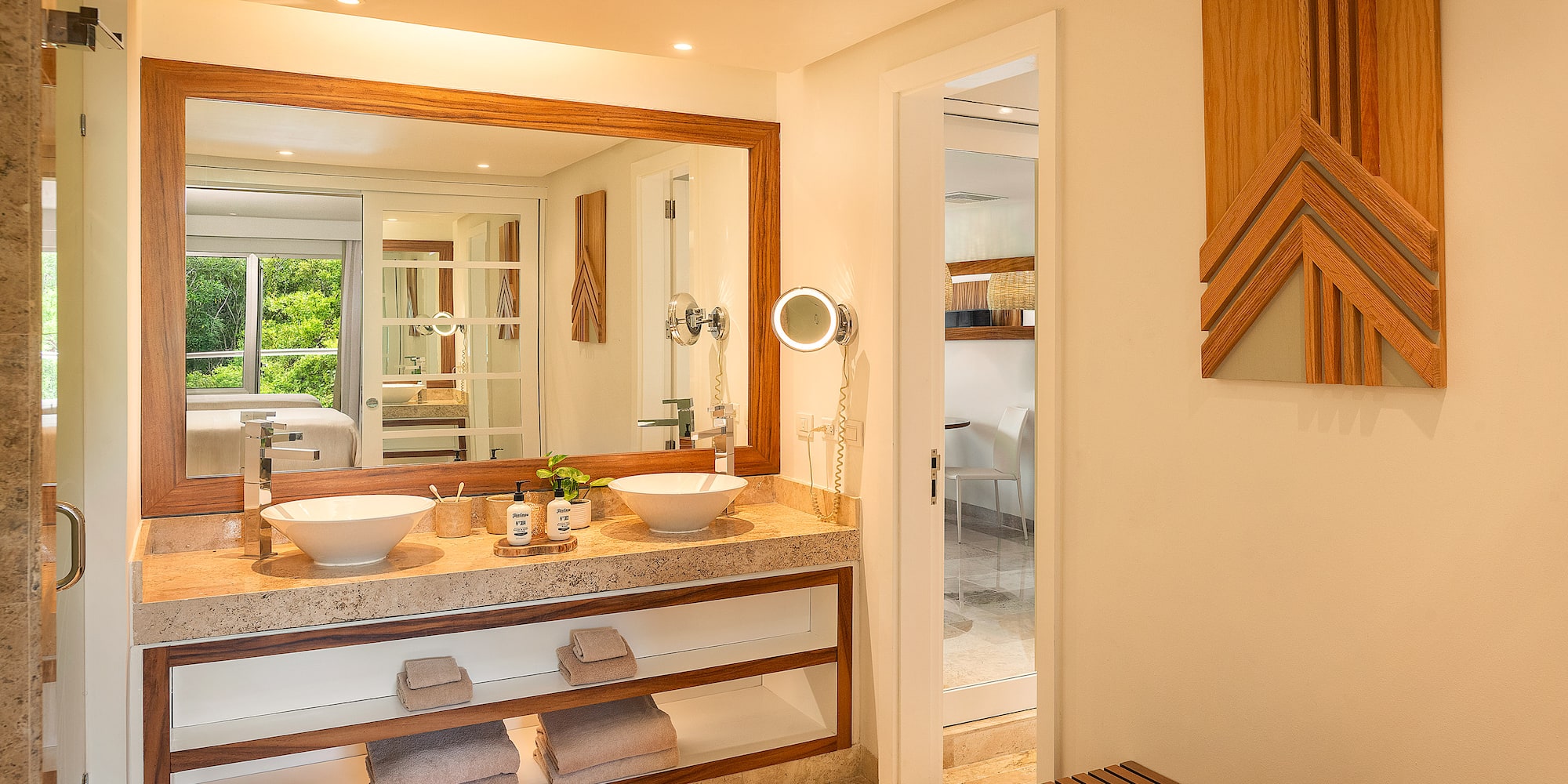 Modern bathroom with double vanity, stone countertop, wood accents, and green view.