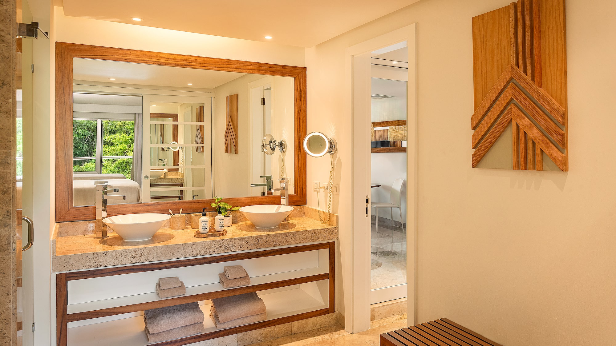 Modern hotel bathroom with double vanity, wood mirror, and stone counter.