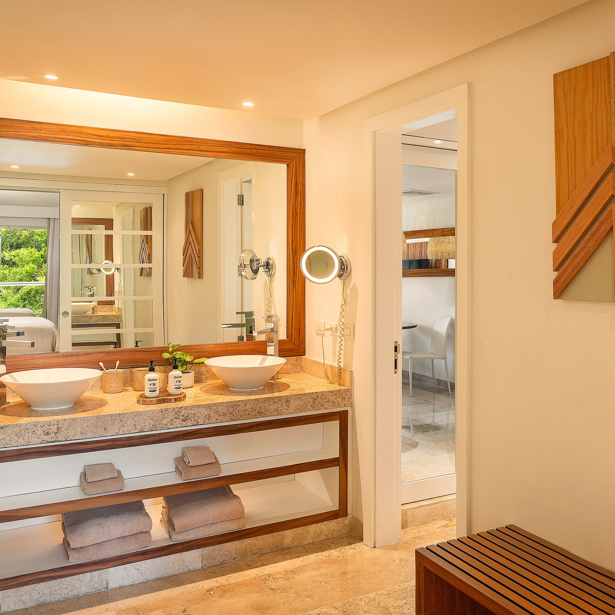 Modern bathroom with double vanity, stone countertop, wood accents, and green view.