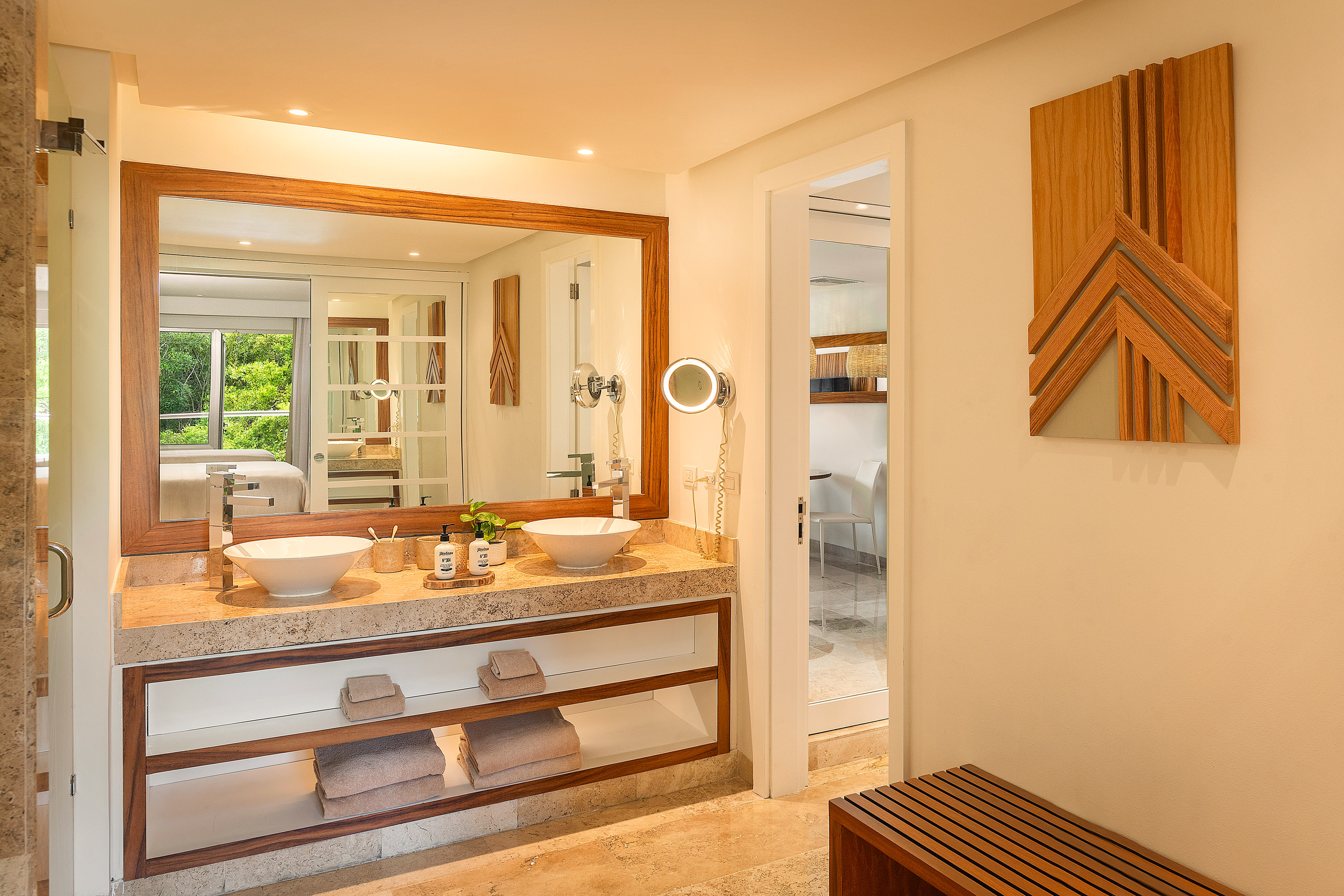 Modern bathroom with double vanity, stone countertop, wood accents, and green view.