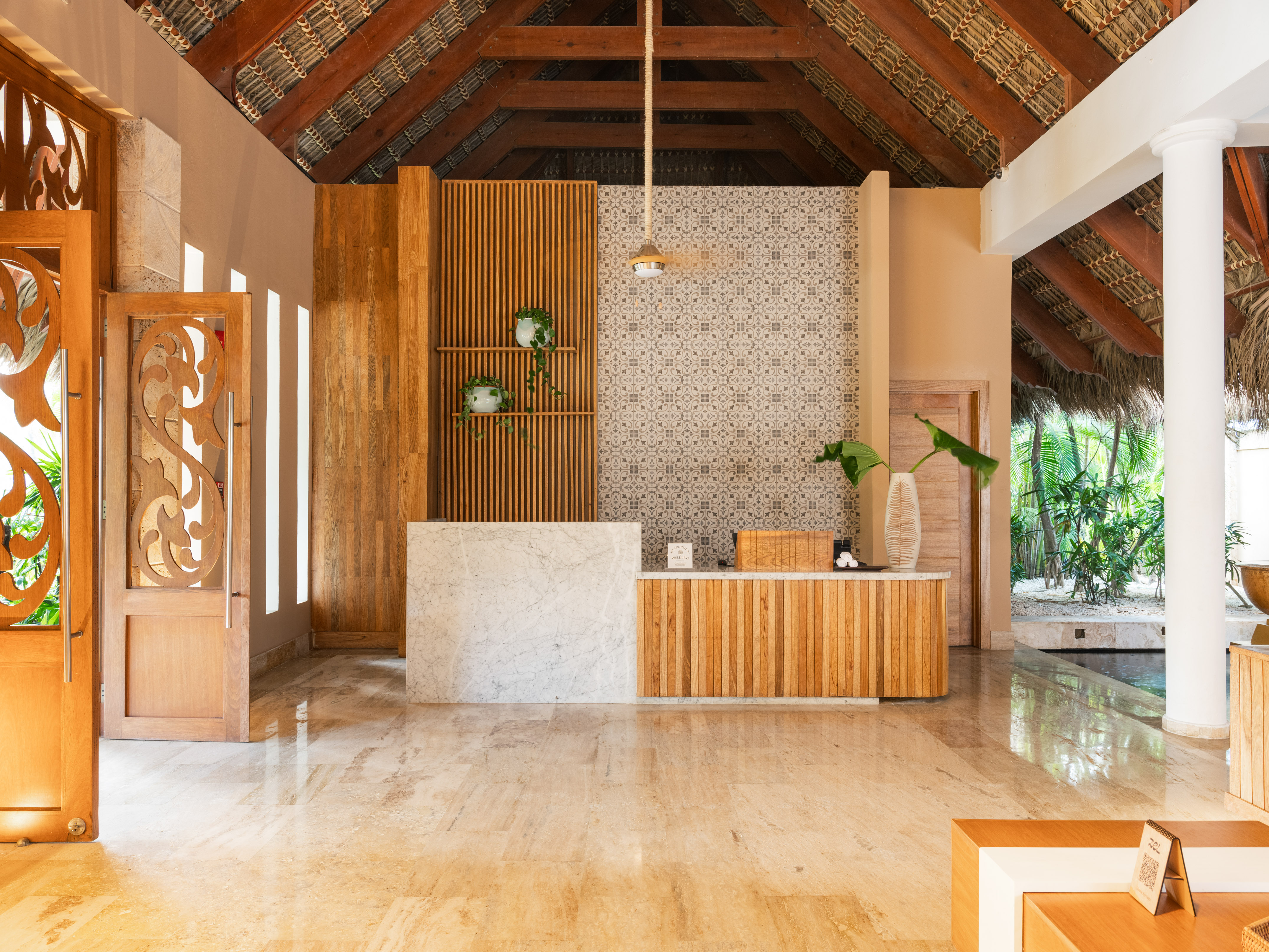 Tropical hotel lobby with marble & wood reception desk, vaulted ceiling.