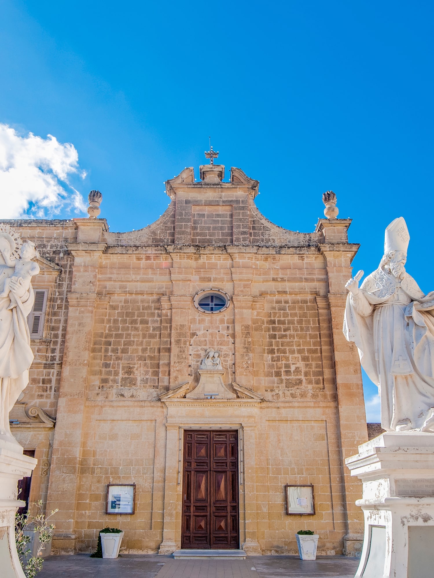 Maltese Baroque church with white saint statues against a blue sky.