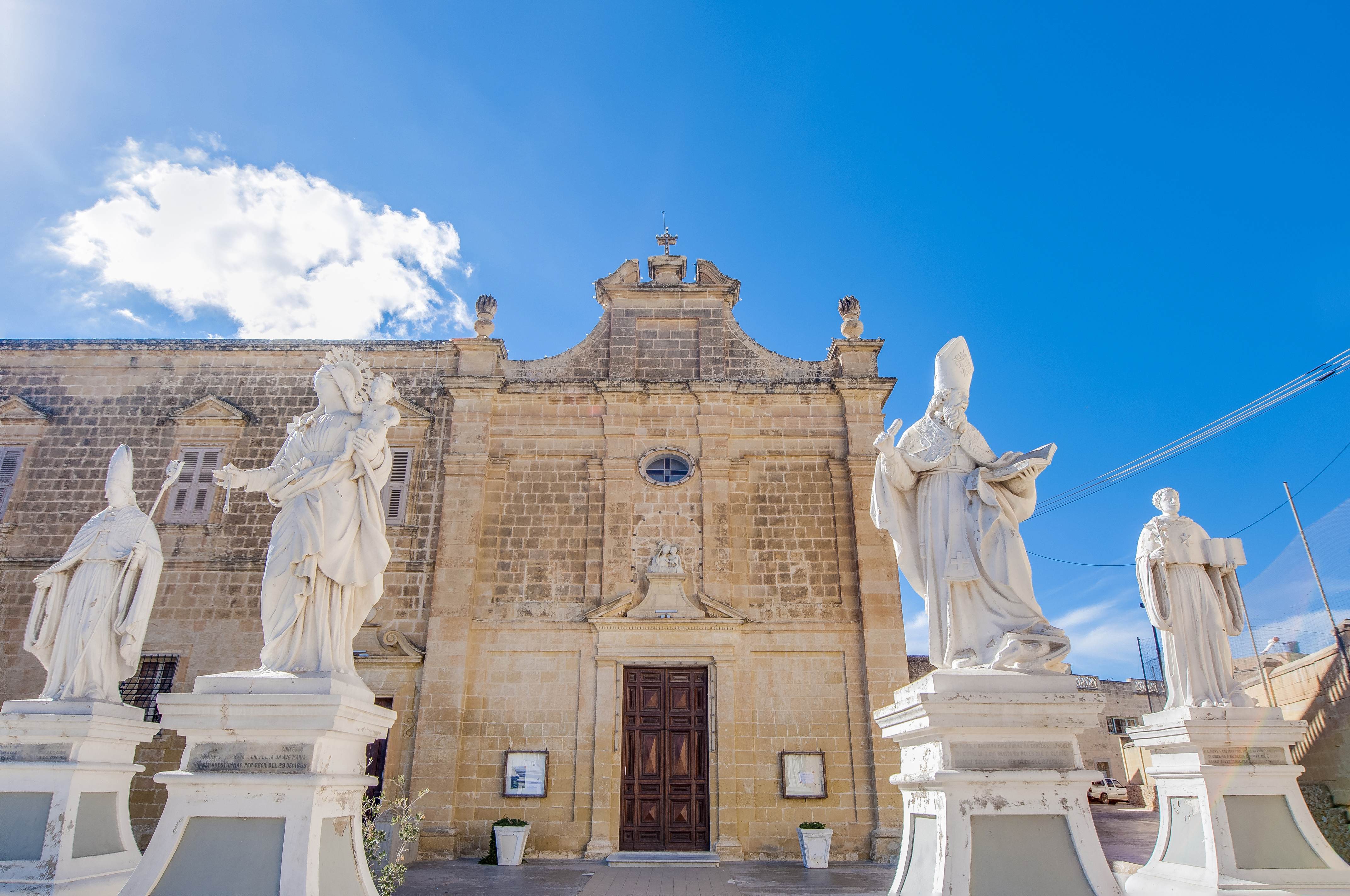 Maltese Baroque church with white saint statues against a blue sky.