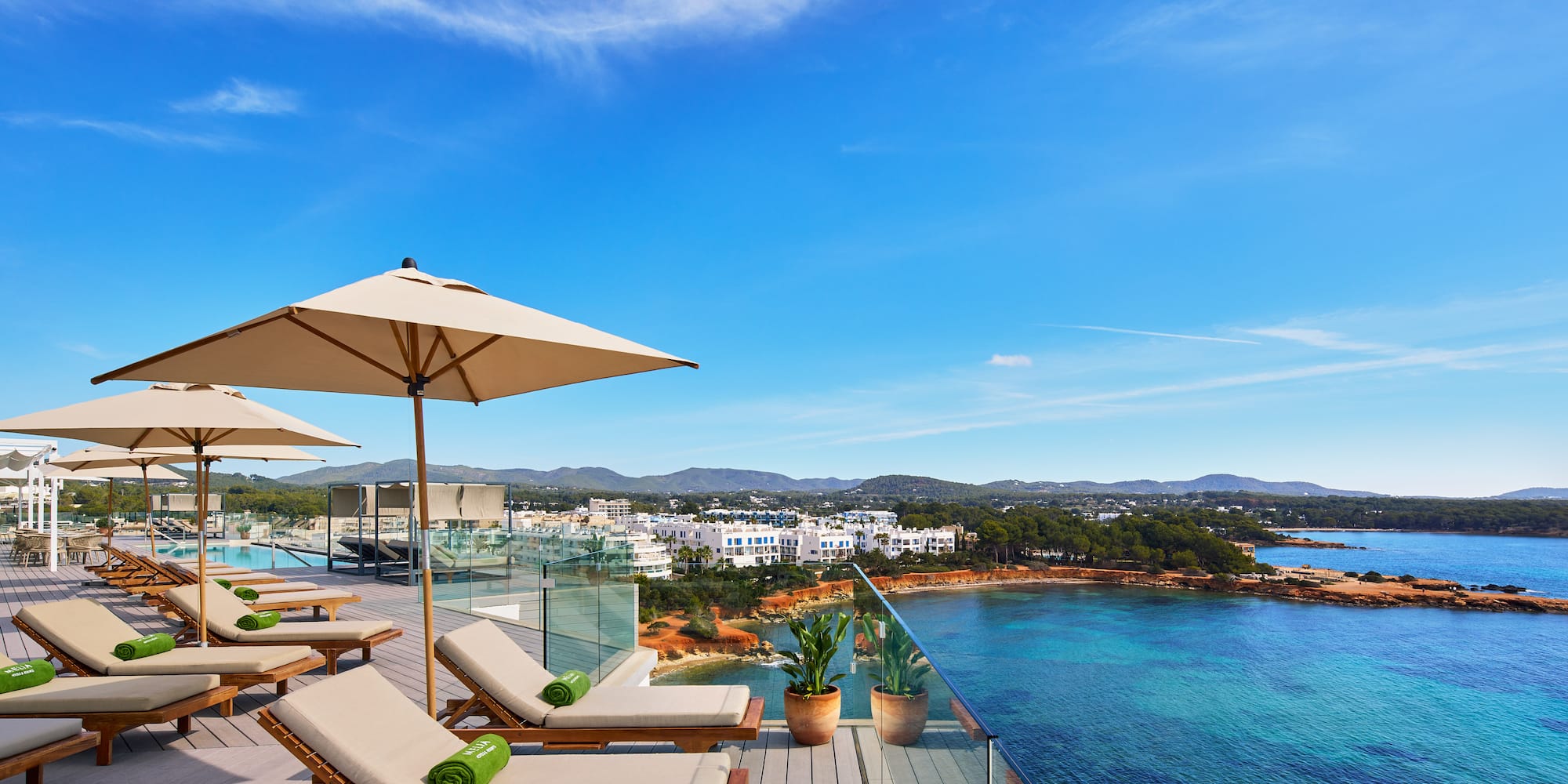 Rooftop terrace with lounge chairs, umbrellas, turquoise sea view, and coastal resort.
