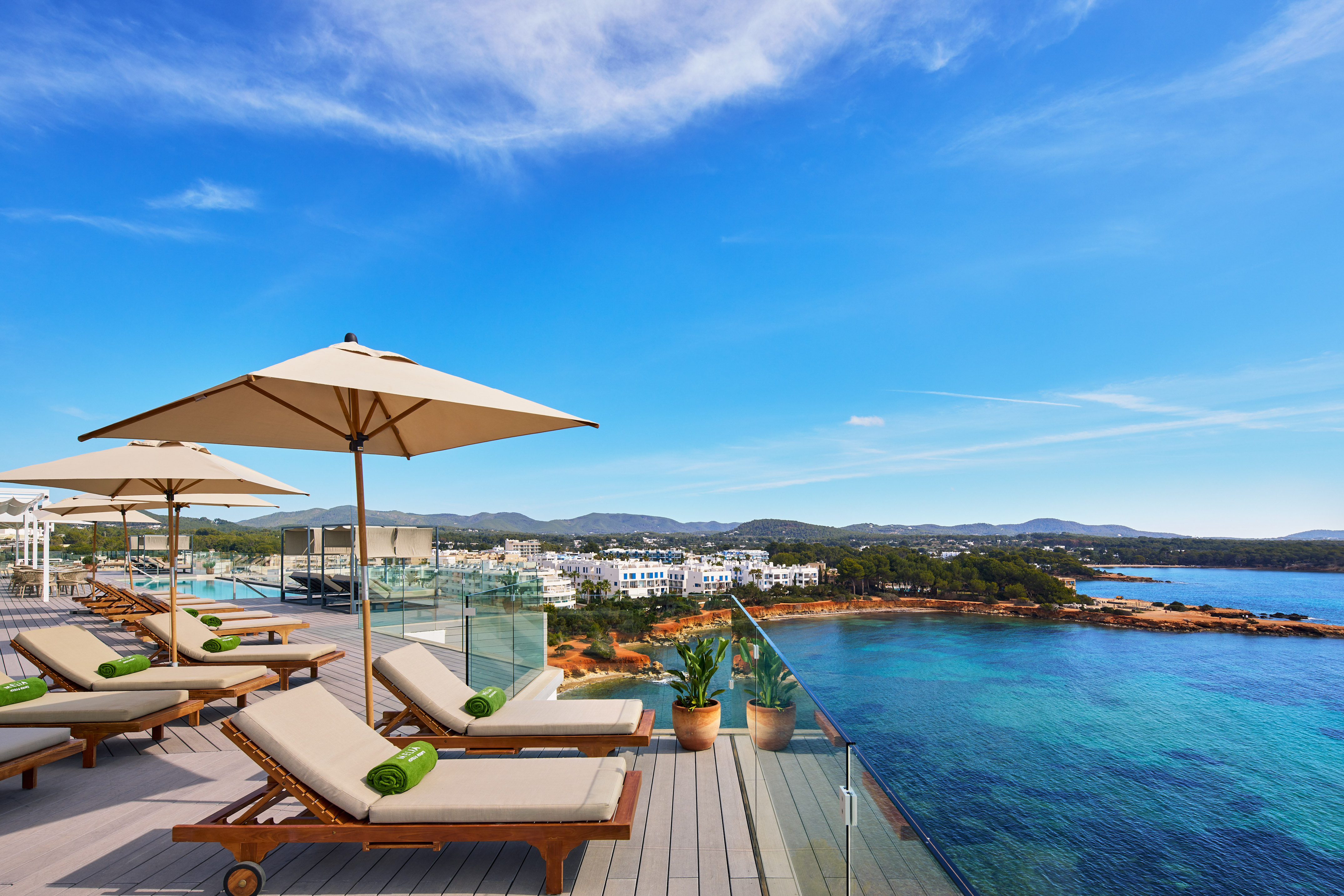 Rooftop terrace with lounge chairs, umbrellas, turquoise sea view, and coastal resort.