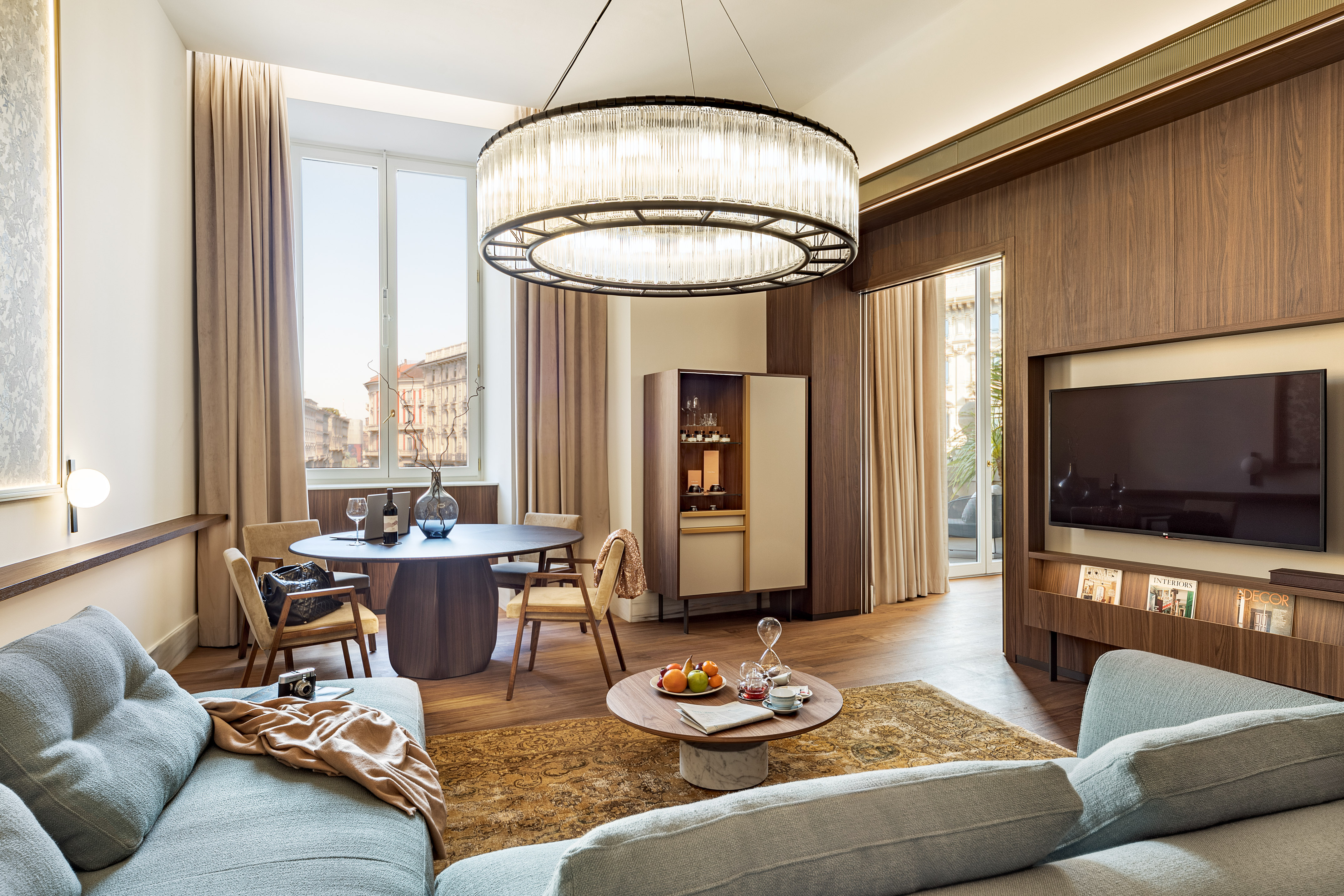 Modern luxury suite with living, dining, large chandelier, and city view.