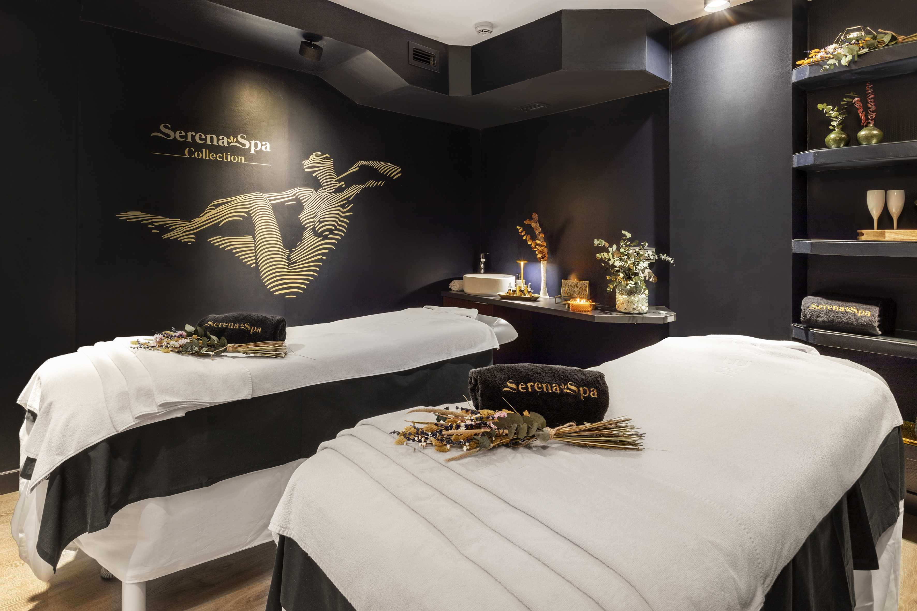 Serena Spa treatment room with two beds, dark walls, and gold logo.