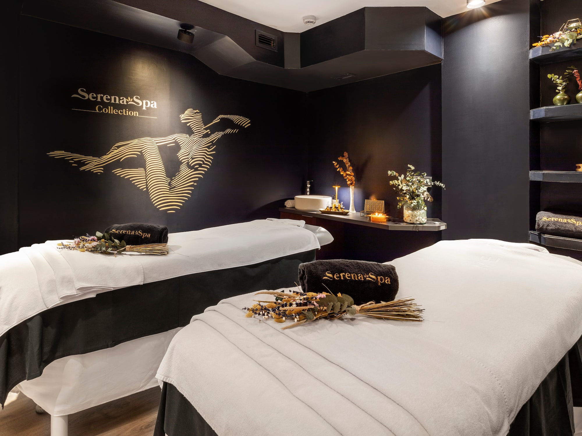 Serena Spa treatment room with two beds, dark walls, and gold logo.