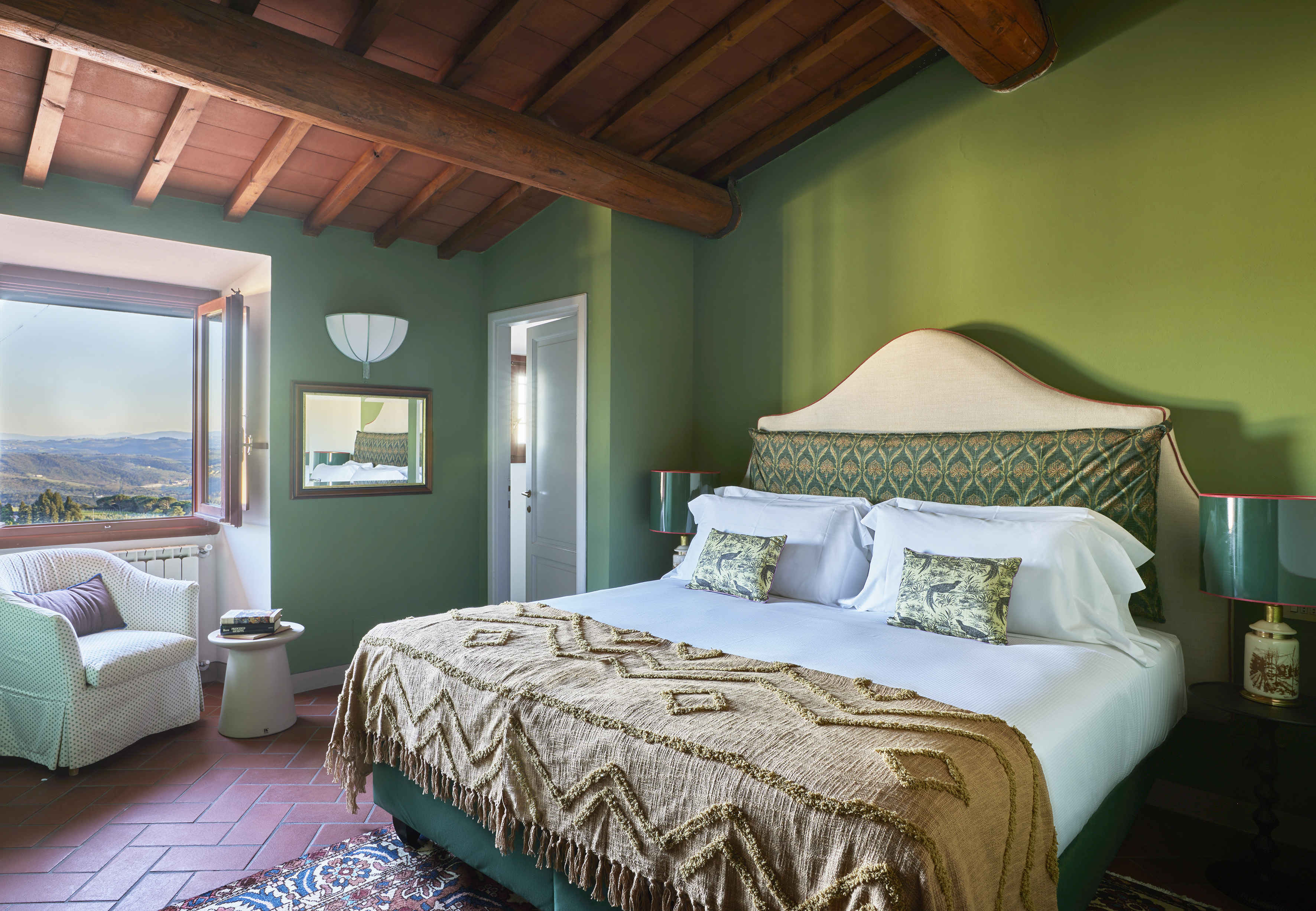 Tuscan style bedroom with green walls, wooden ceiling, and scenic window view.