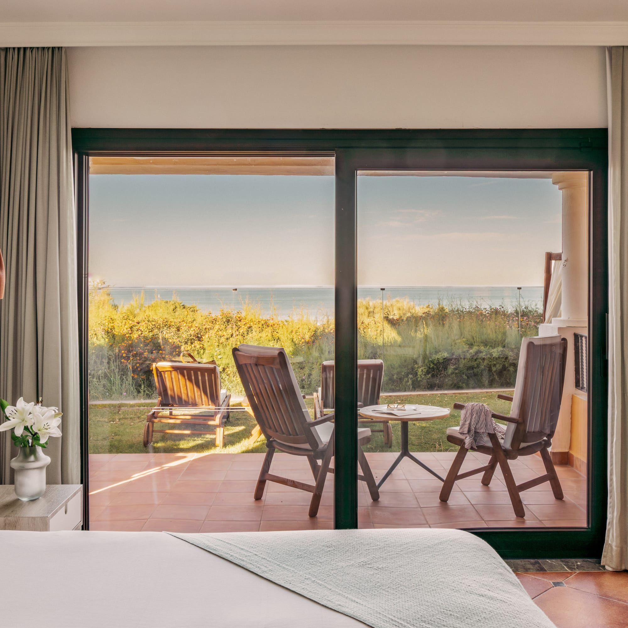 Hotel bedroom with glass doors opening to a patio and ocean view.