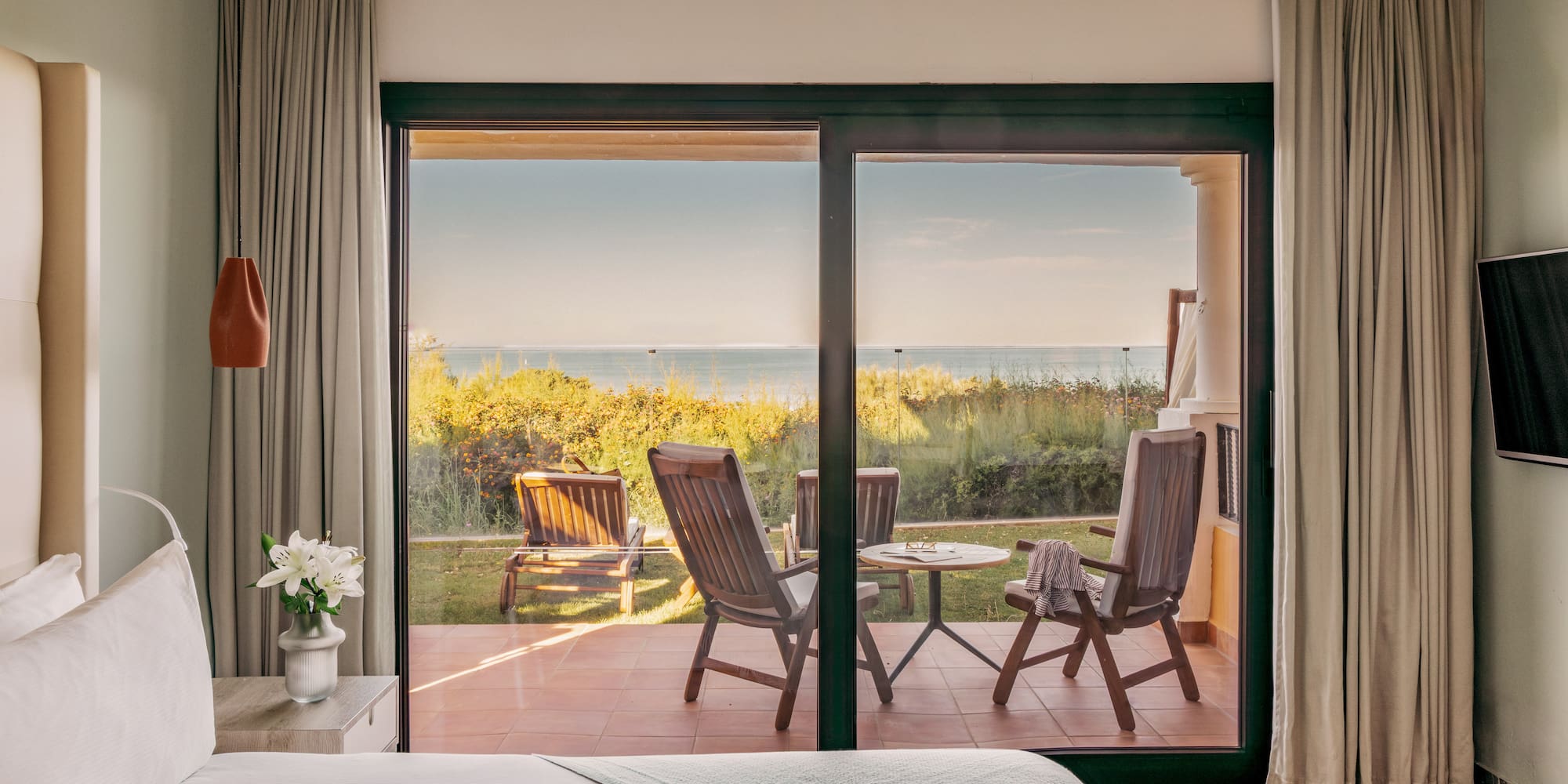Hotel bedroom with glass doors opening to a patio and ocean view.