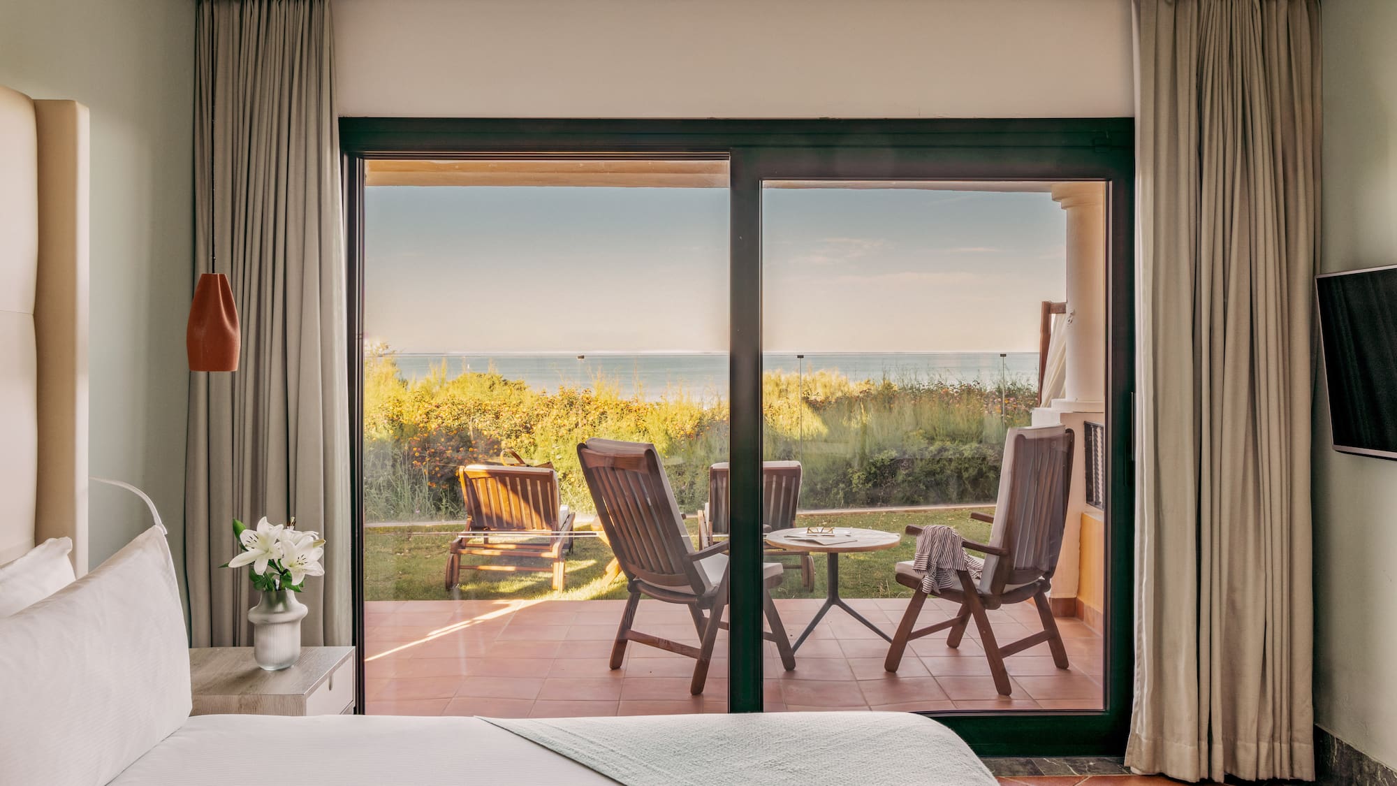 Hotel bedroom with glass doors opening to a patio and ocean view.