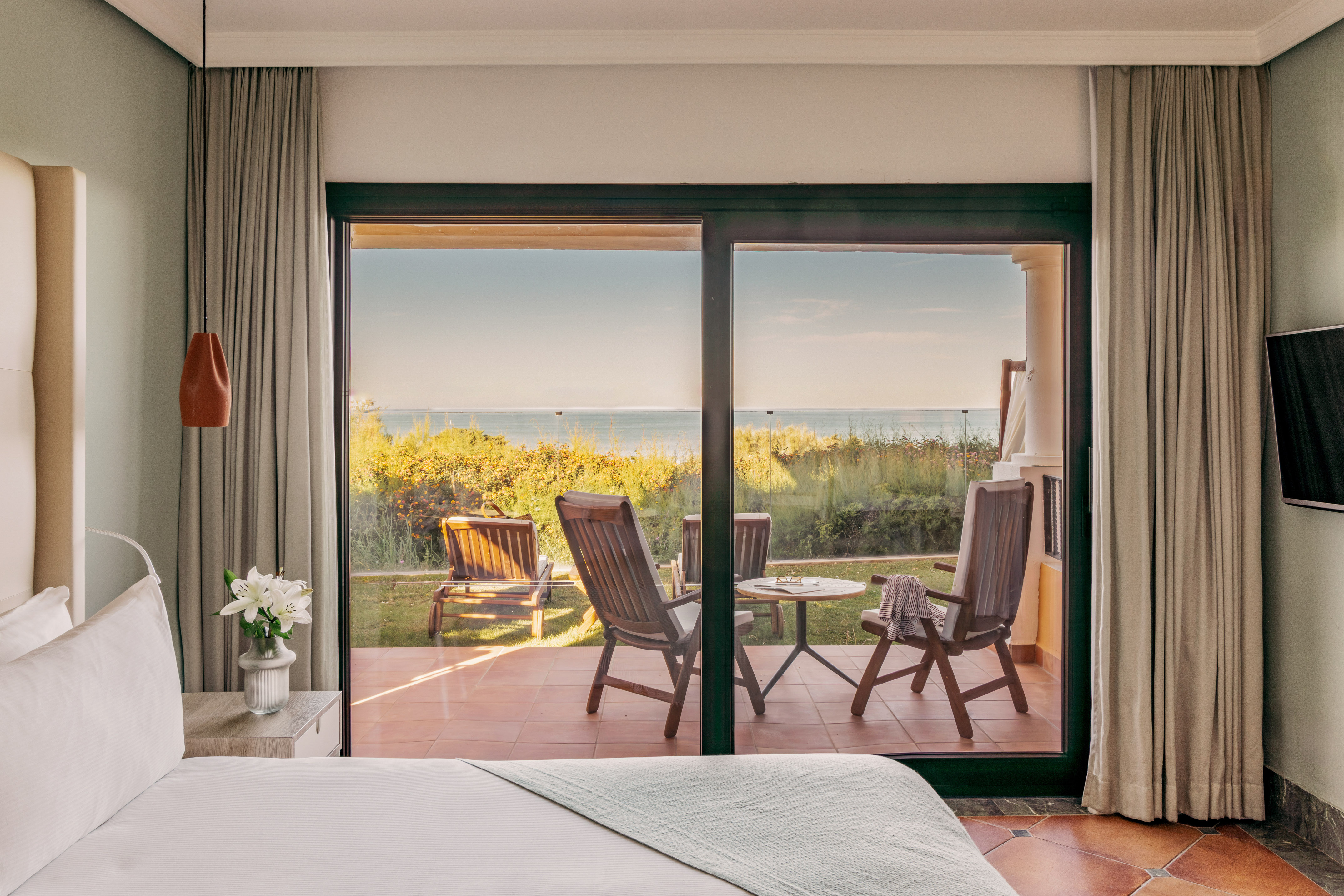 Hotel bedroom with glass doors opening to a patio and ocean view.