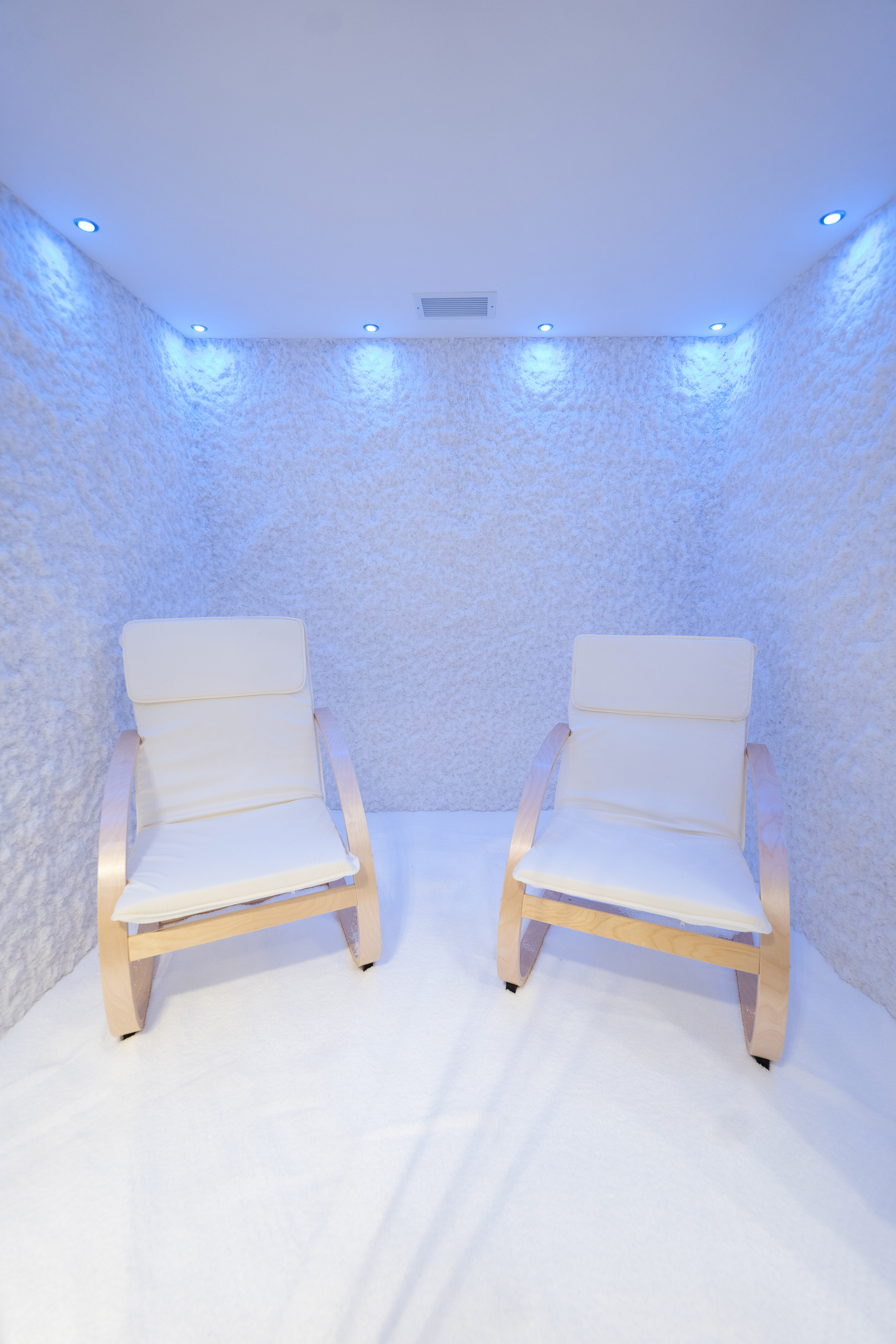 Halotherapy room with two white chairs, textured salt walls, and blue lights.
