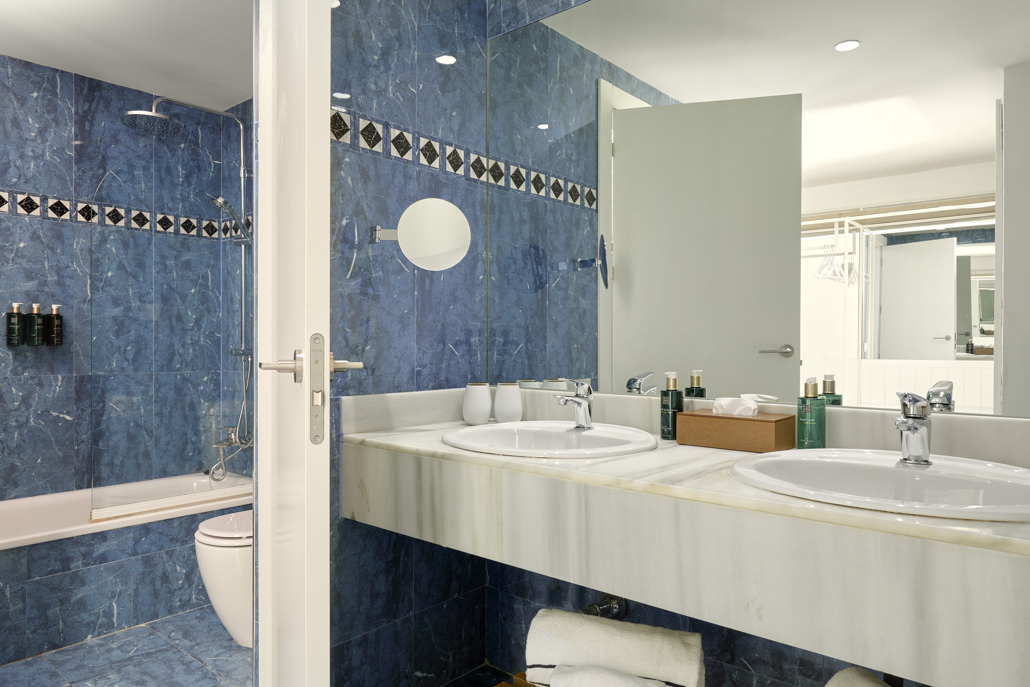Modern hotel bathroom with blue tiles, double vanity, shower, and bathtub.