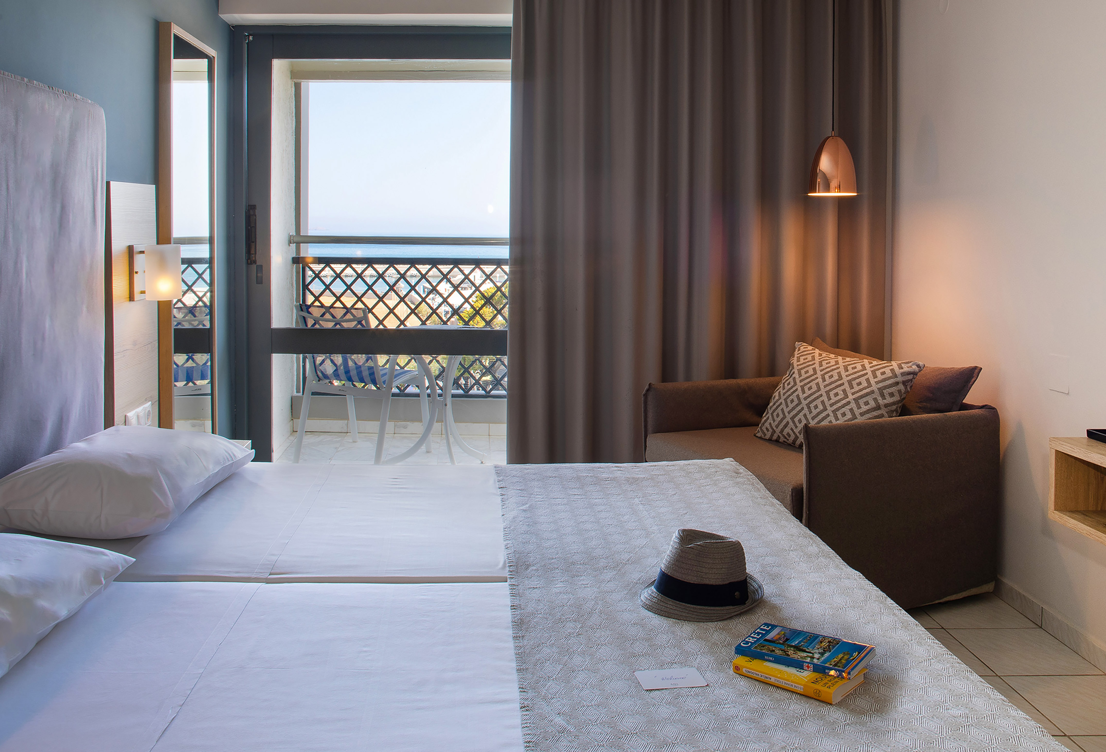 Crete hotel room with balcony sea view, twin beds, and sofa.