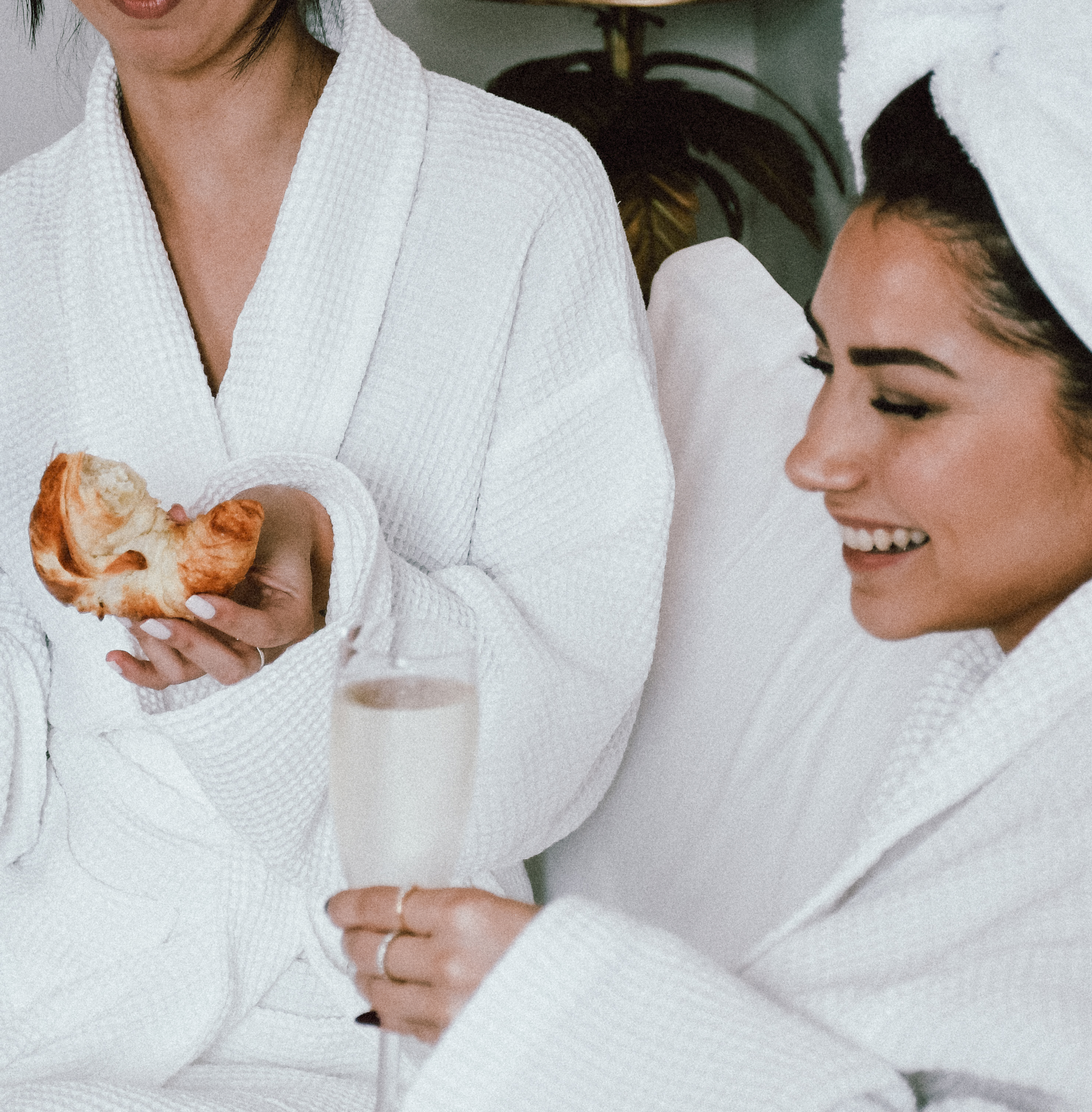 Two women in white robes are holding a pastry.