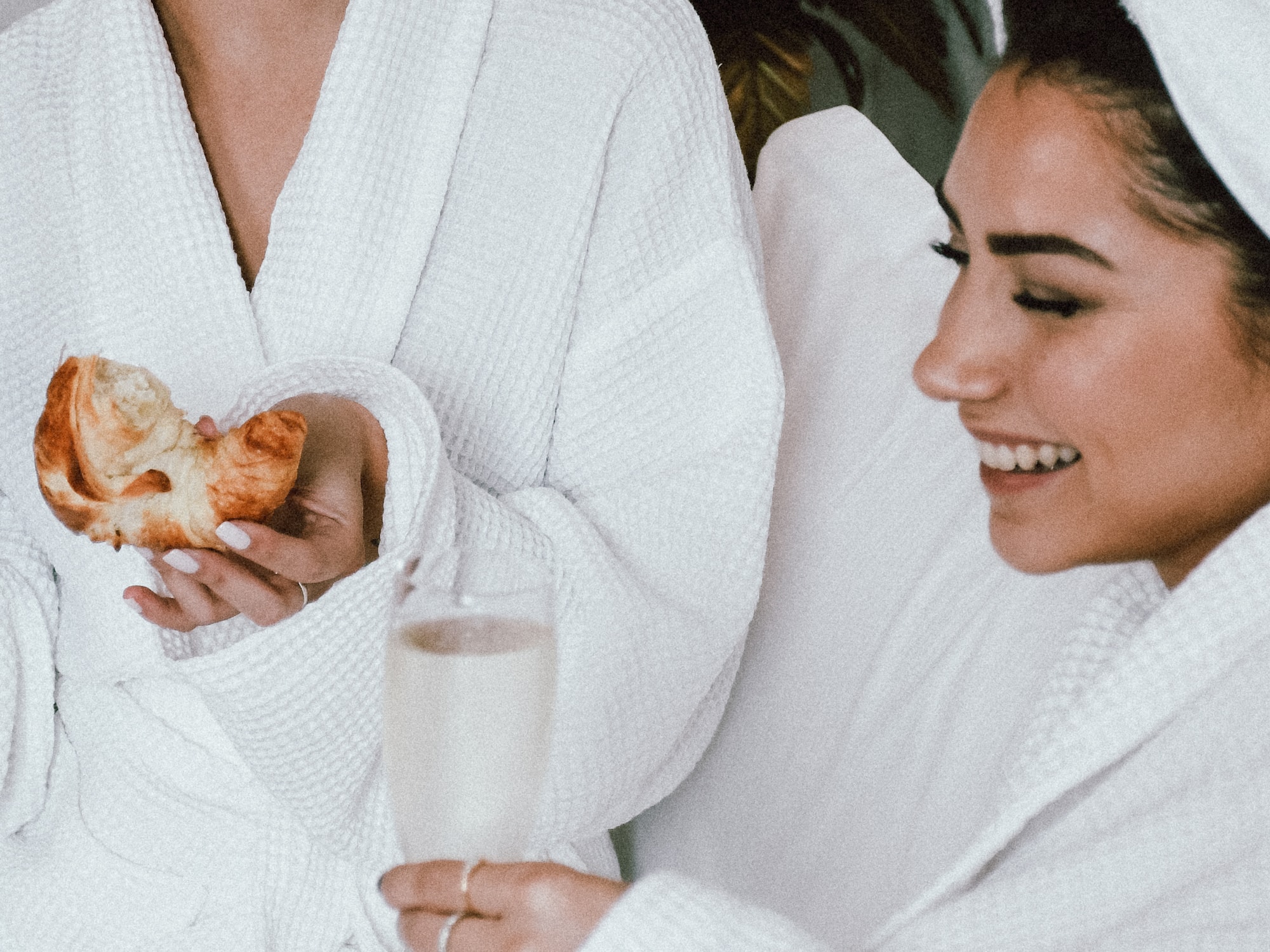 Two women in white robes are holding a pastry.