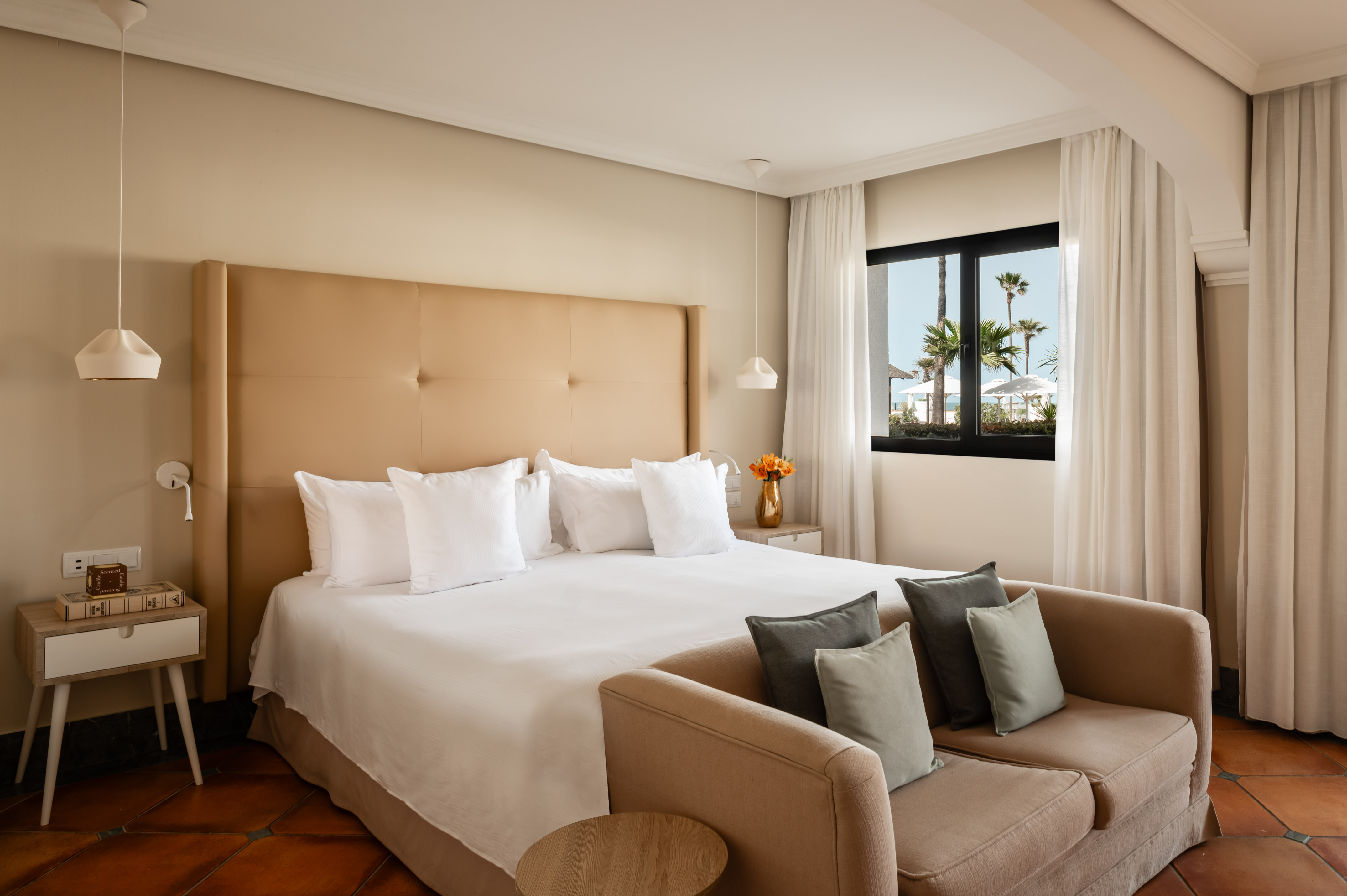 Modern hotel bedroom with large bed, sofa, and window beach view.