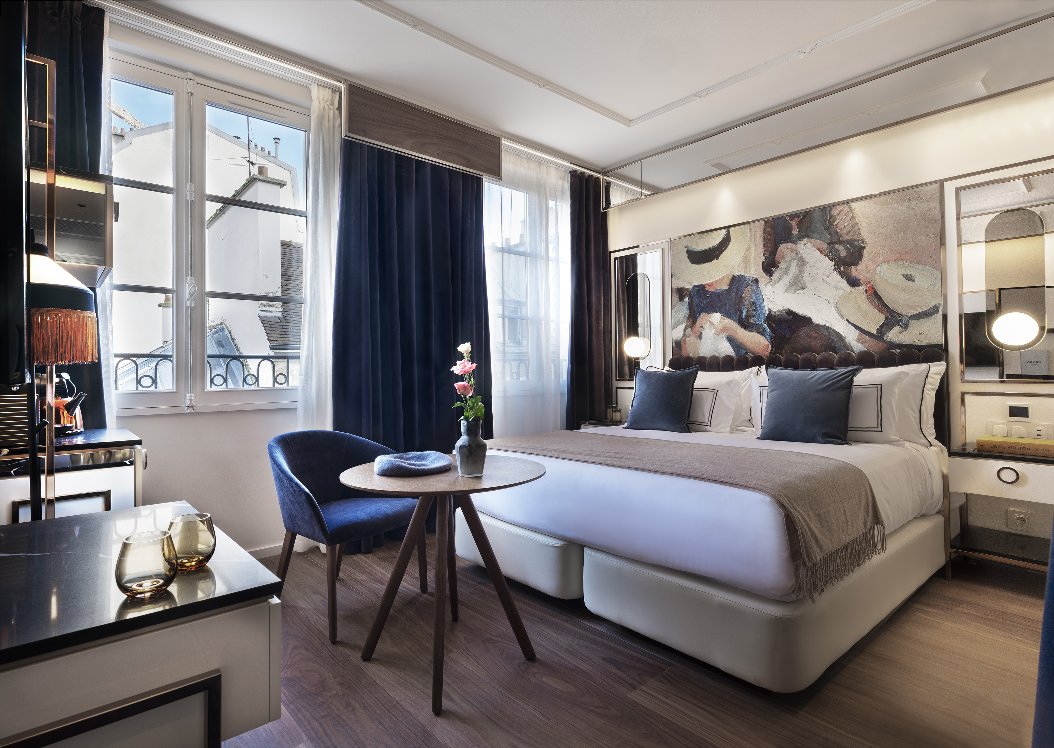 Modern luxury hotel room with abstract art, large bed, and city view window.