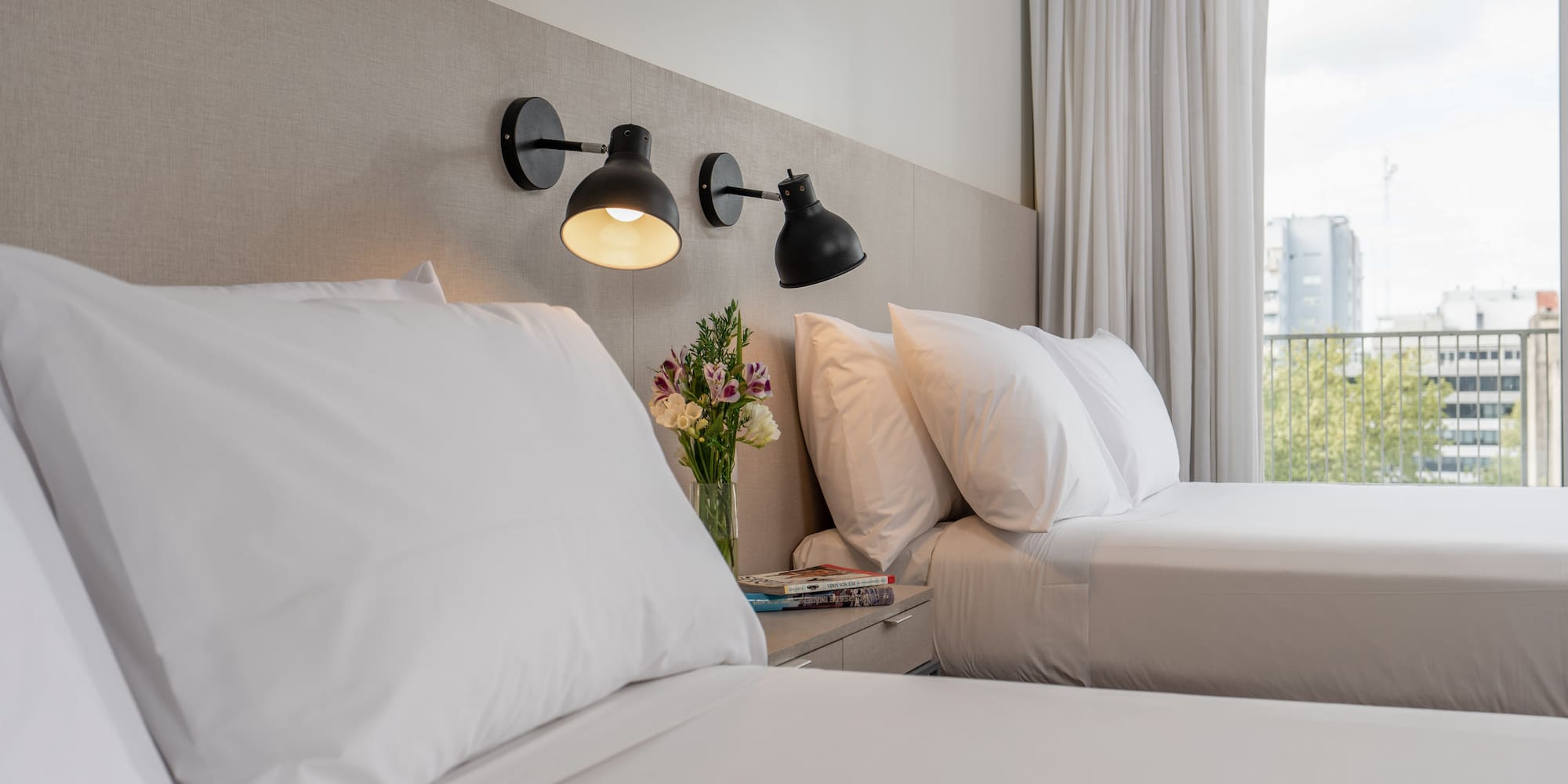 a bed with white sheets and a vase of flowers on a table