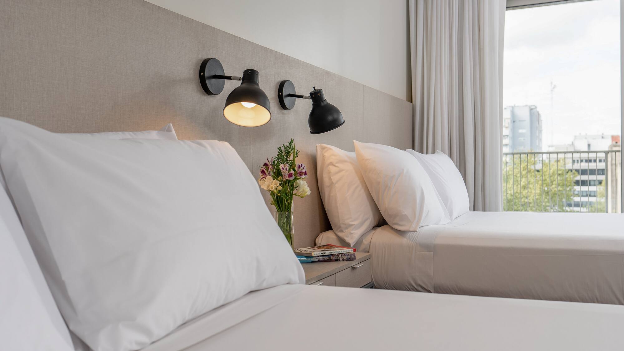 a bed with white sheets and a vase of flowers on a table