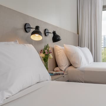 a bed with white sheets and a vase of flowers on a table