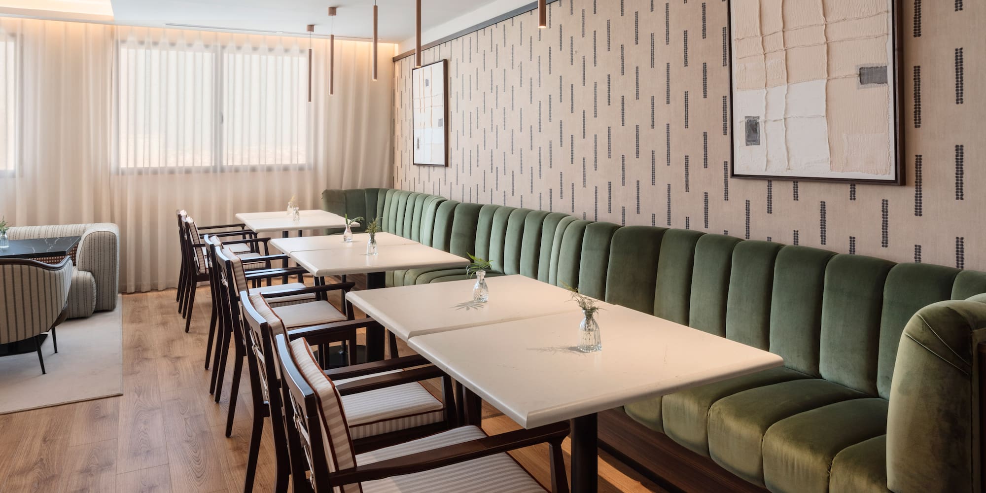 Interior de restaurante moderno con asientos verdes de terciopelo y mesas blancas.