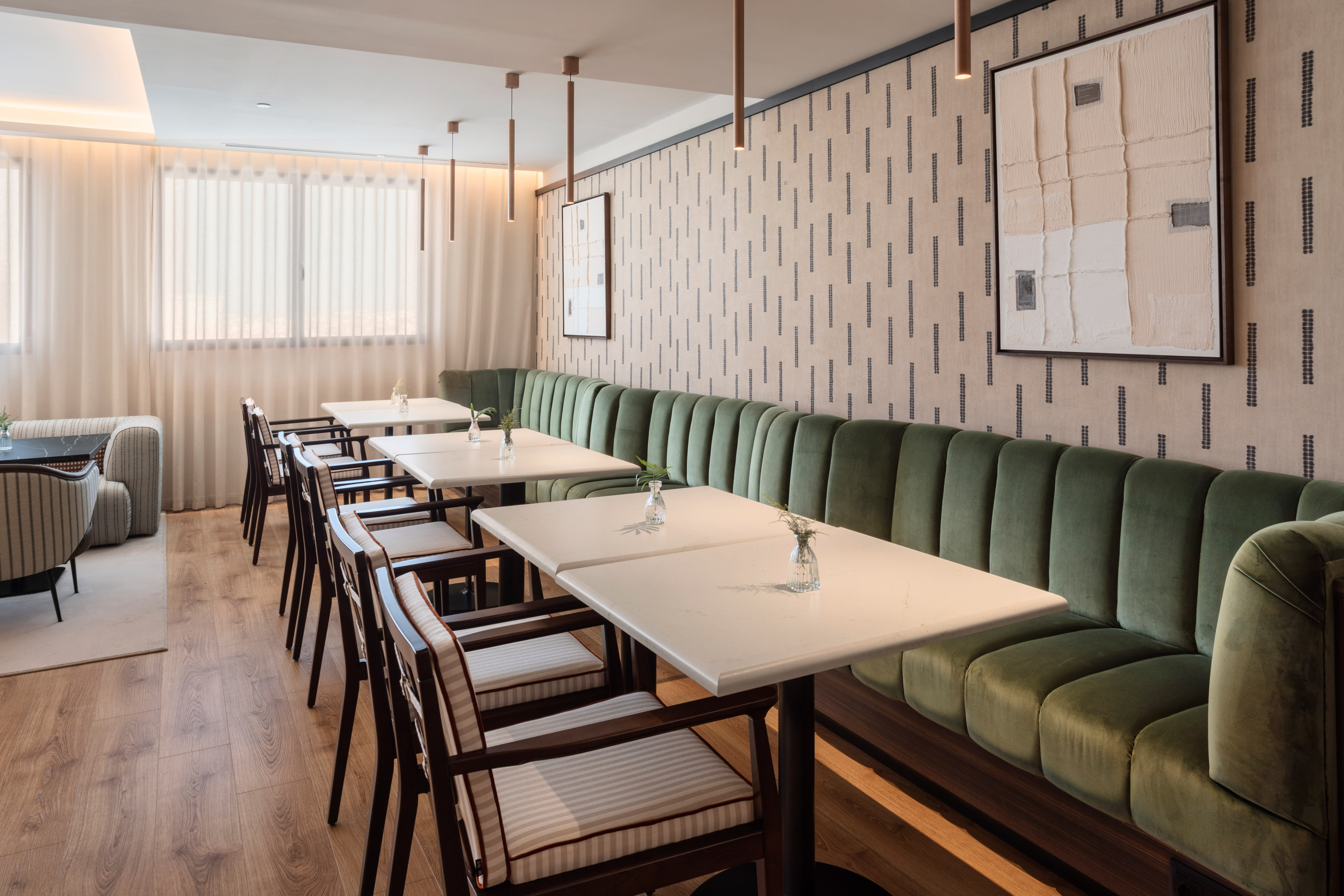 Interior de restaurante moderno con asientos verdes de terciopelo y mesas blancas.