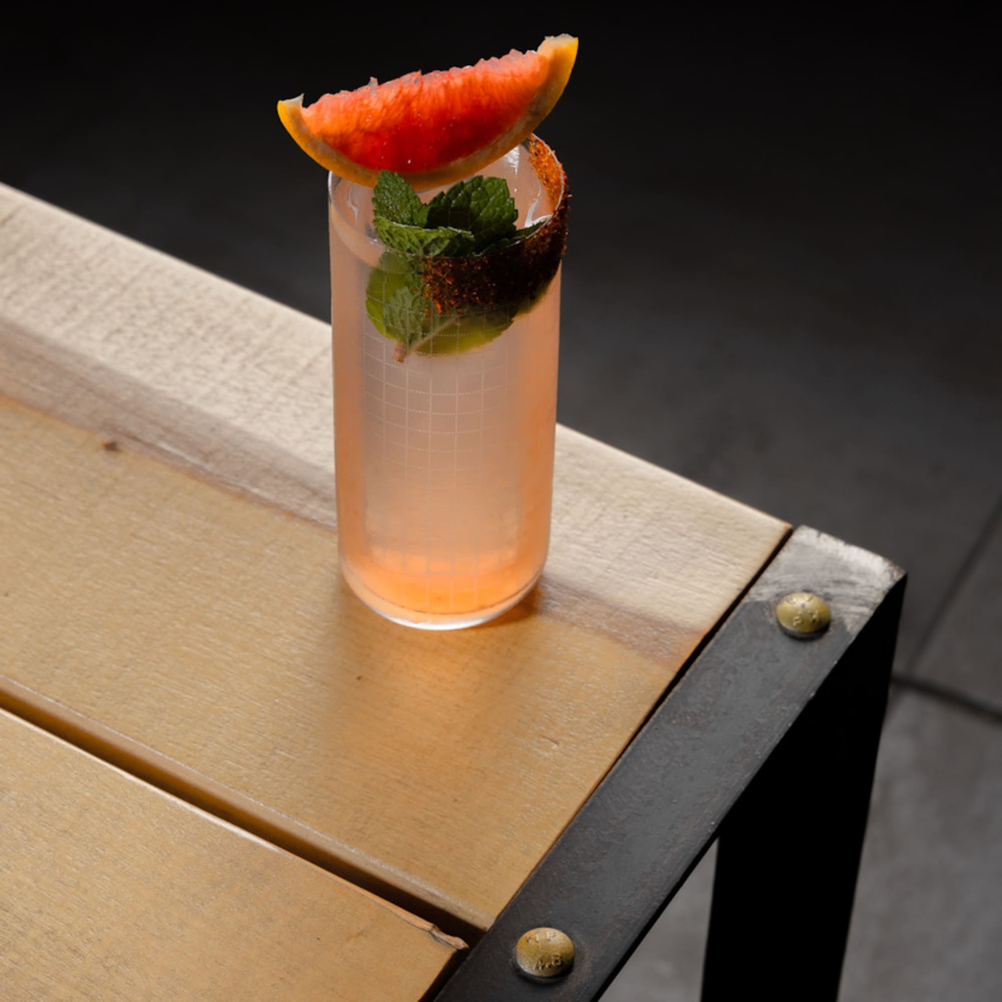 a glass of pink drink with a slice of grapefruit on top of a wooden table