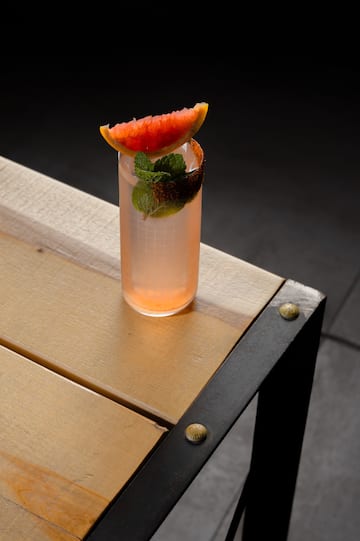 a glass of pink drink with a slice of grapefruit on top of a wooden table