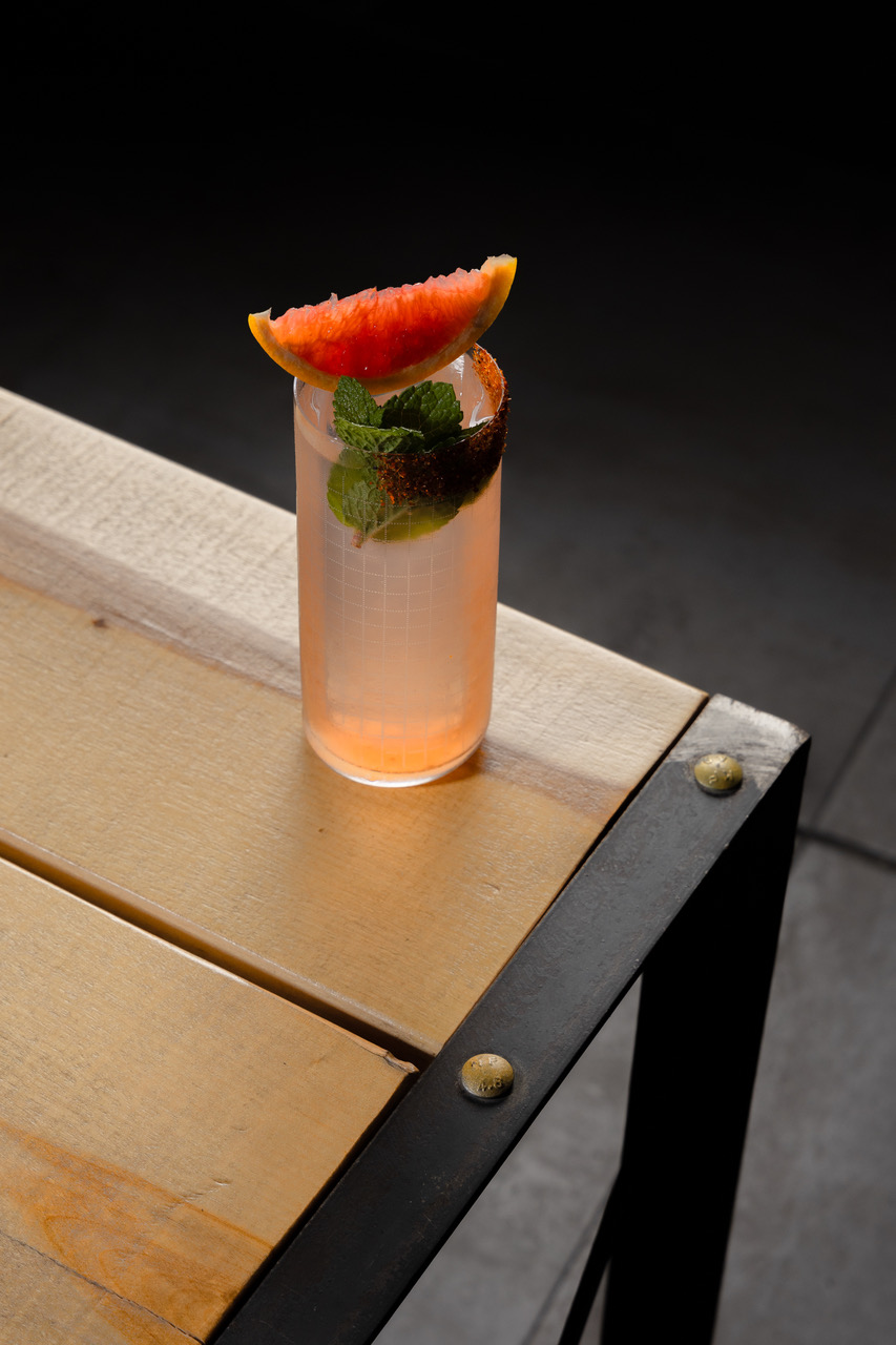 a glass of pink drink with a slice of grapefruit on top of a wooden table