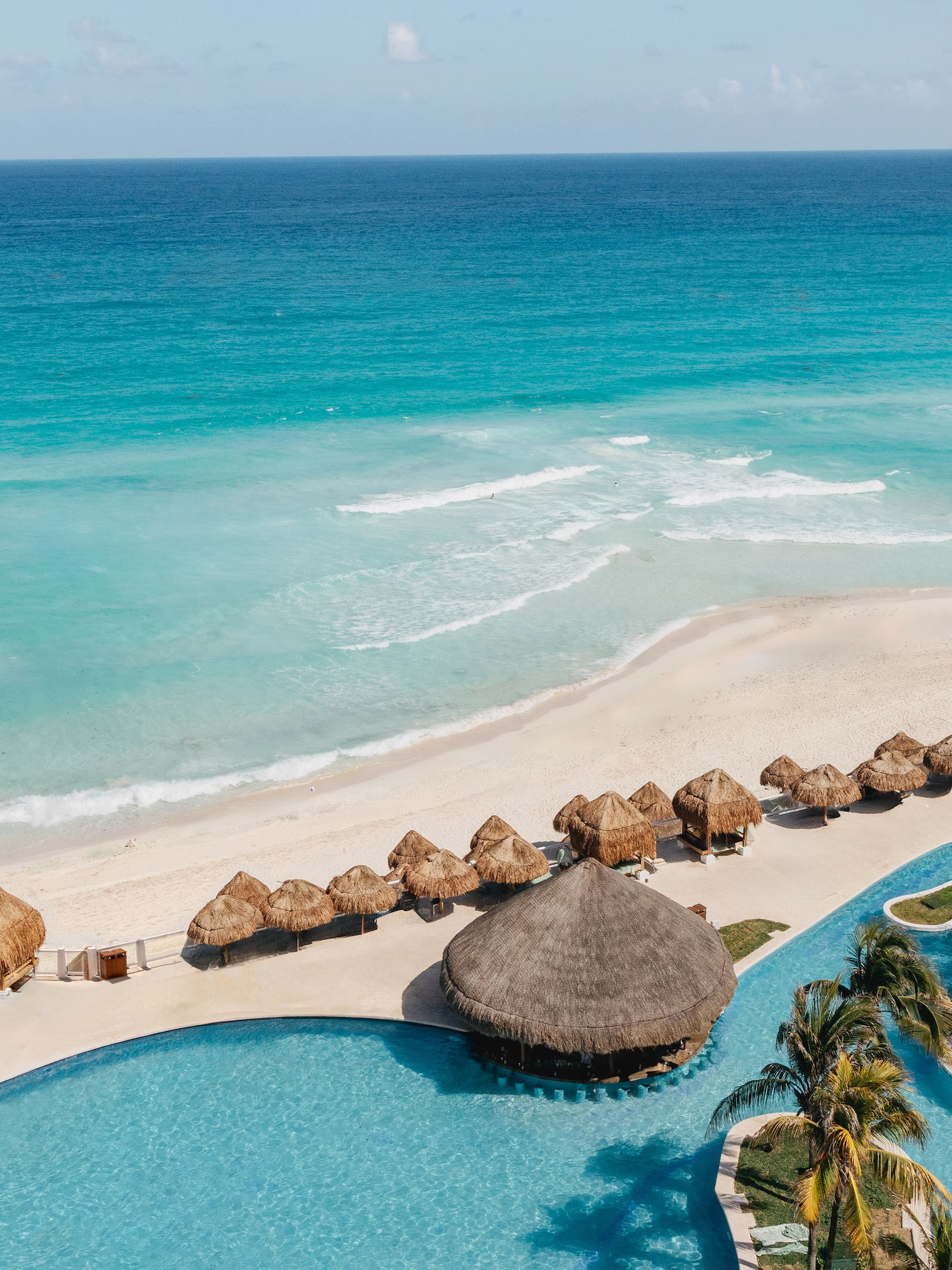 Aerial view: Tropical beach resort with ocean, white sand, pool, and thatched palapas.