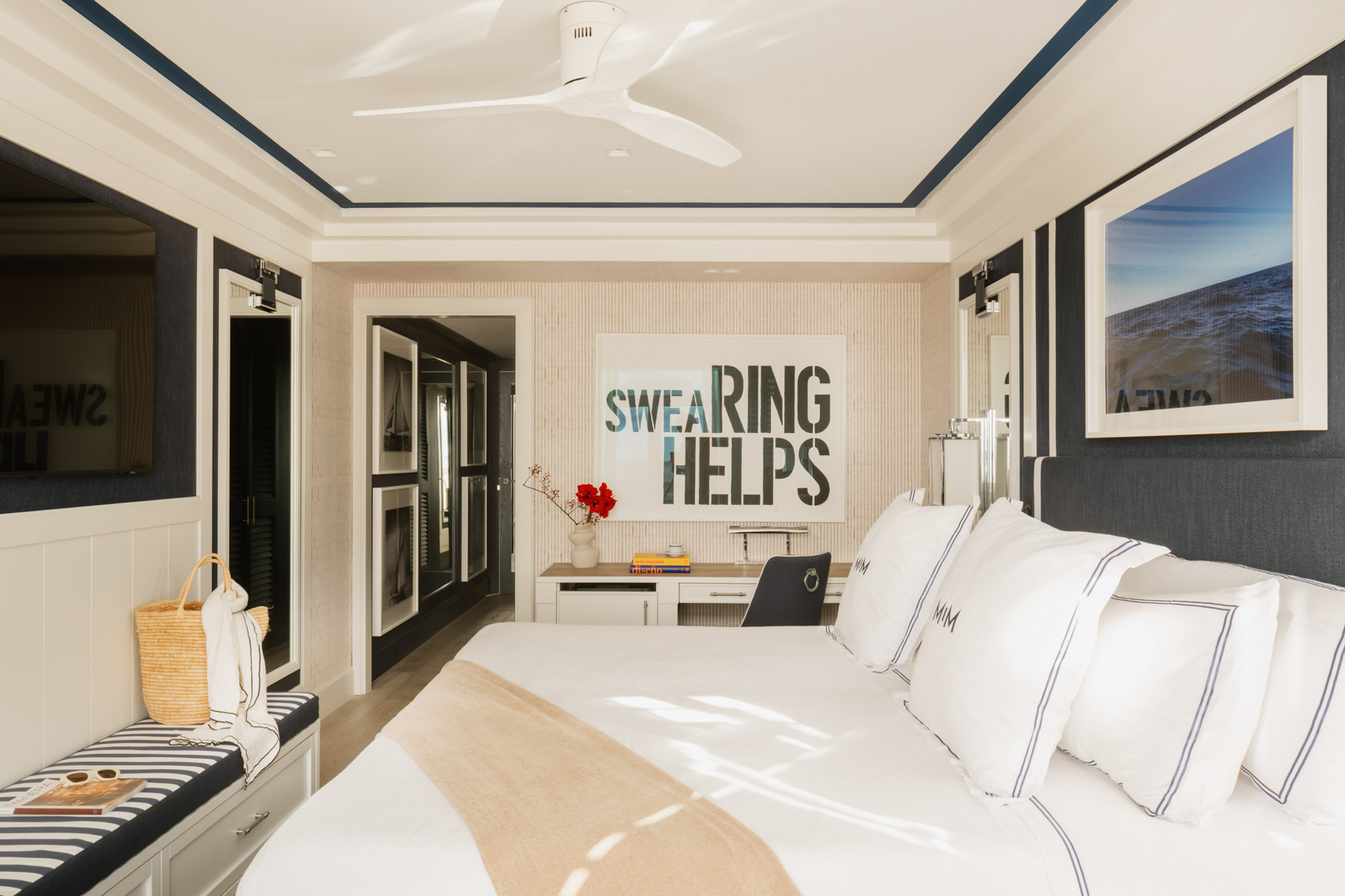 Stylish coastal bedroom with white bed, blue stripes, desk, and modern wall art.