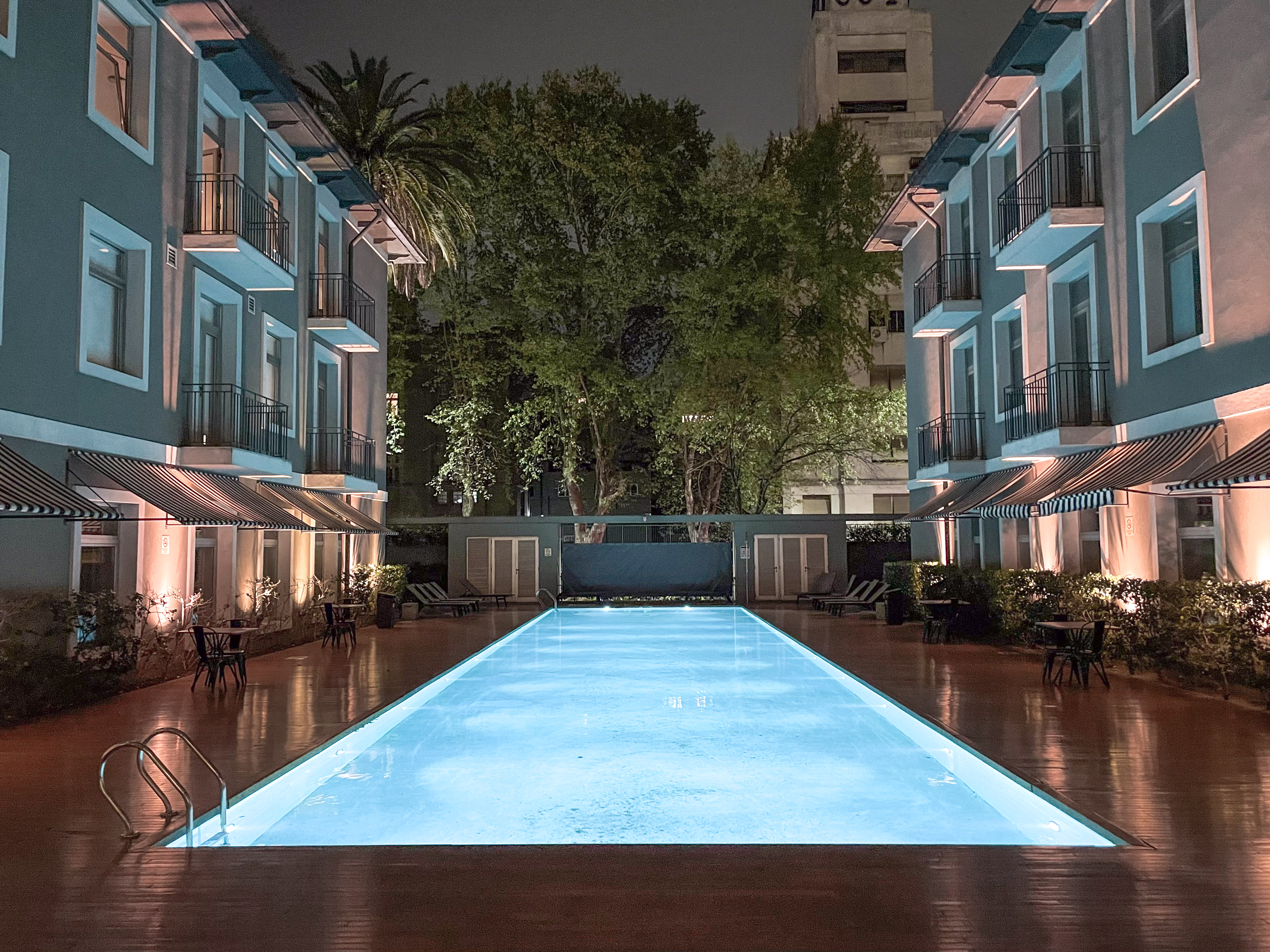 Modern hotel courtyard with illuminated blue swimming pool at night.