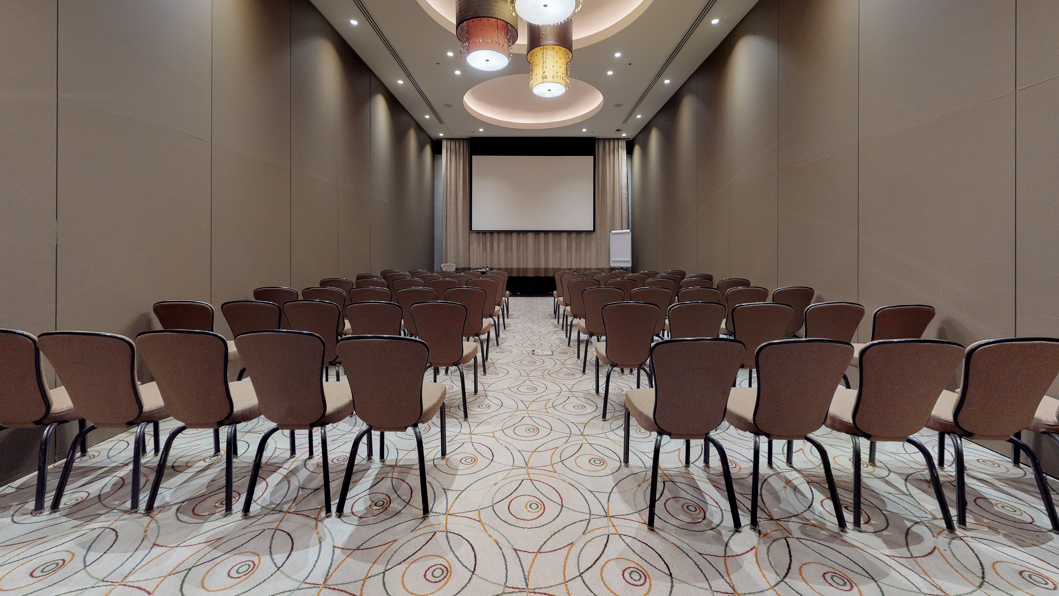 Modern meeting room with theater seating, large screen, and patterned carpet.