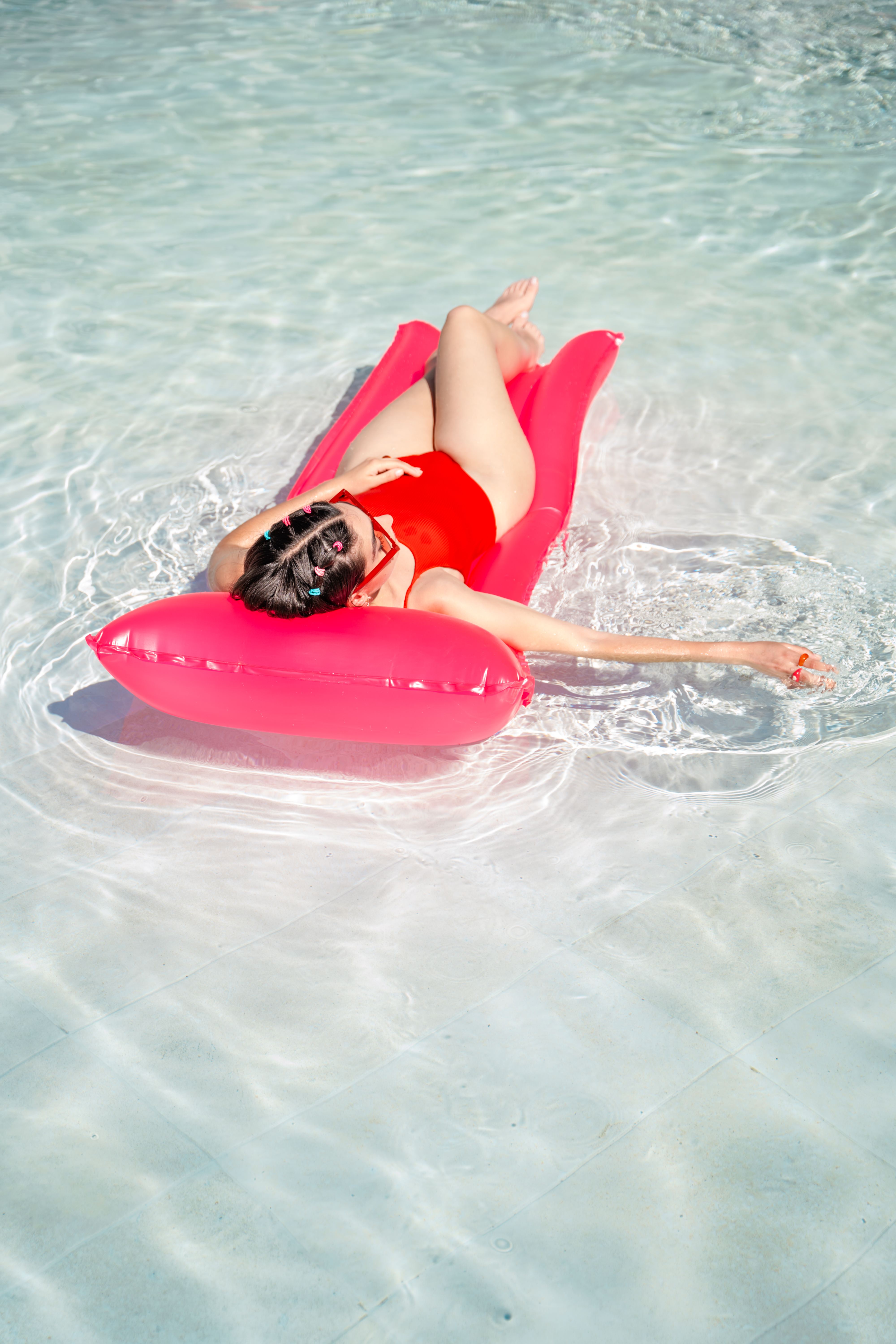 Woman in red swimsuit floating on pink raft in sunny swimming pool.