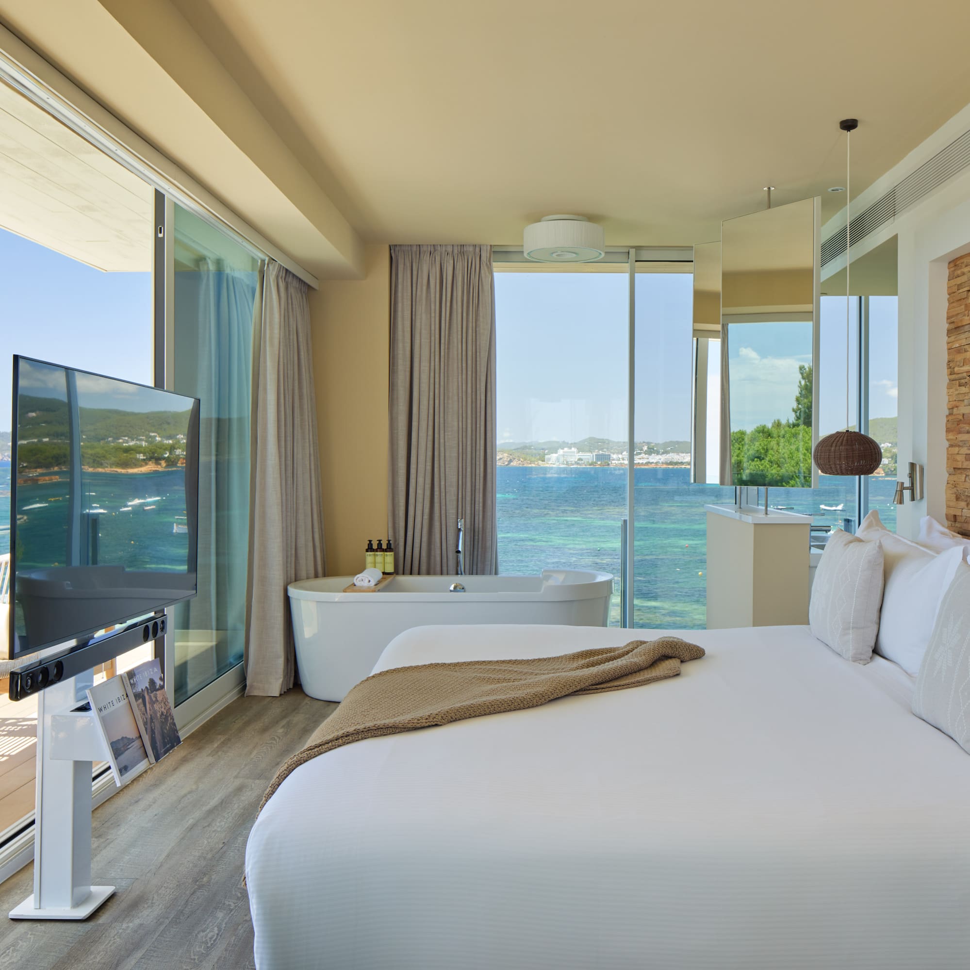 Luxury ocean view hotel suite with bed, freestanding tub, and balcony.