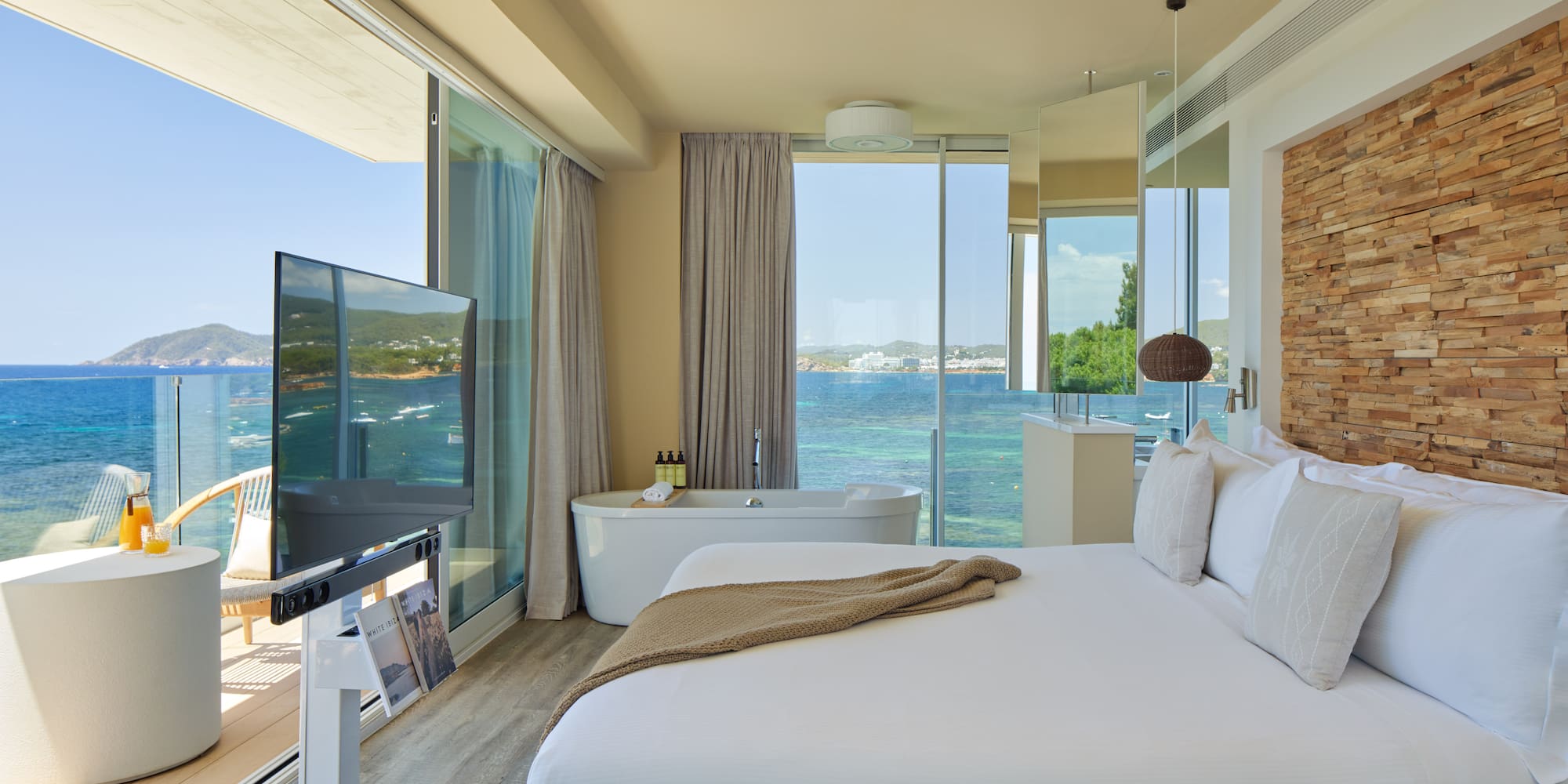 Luxury ocean view hotel suite with bed, freestanding tub, and balcony.