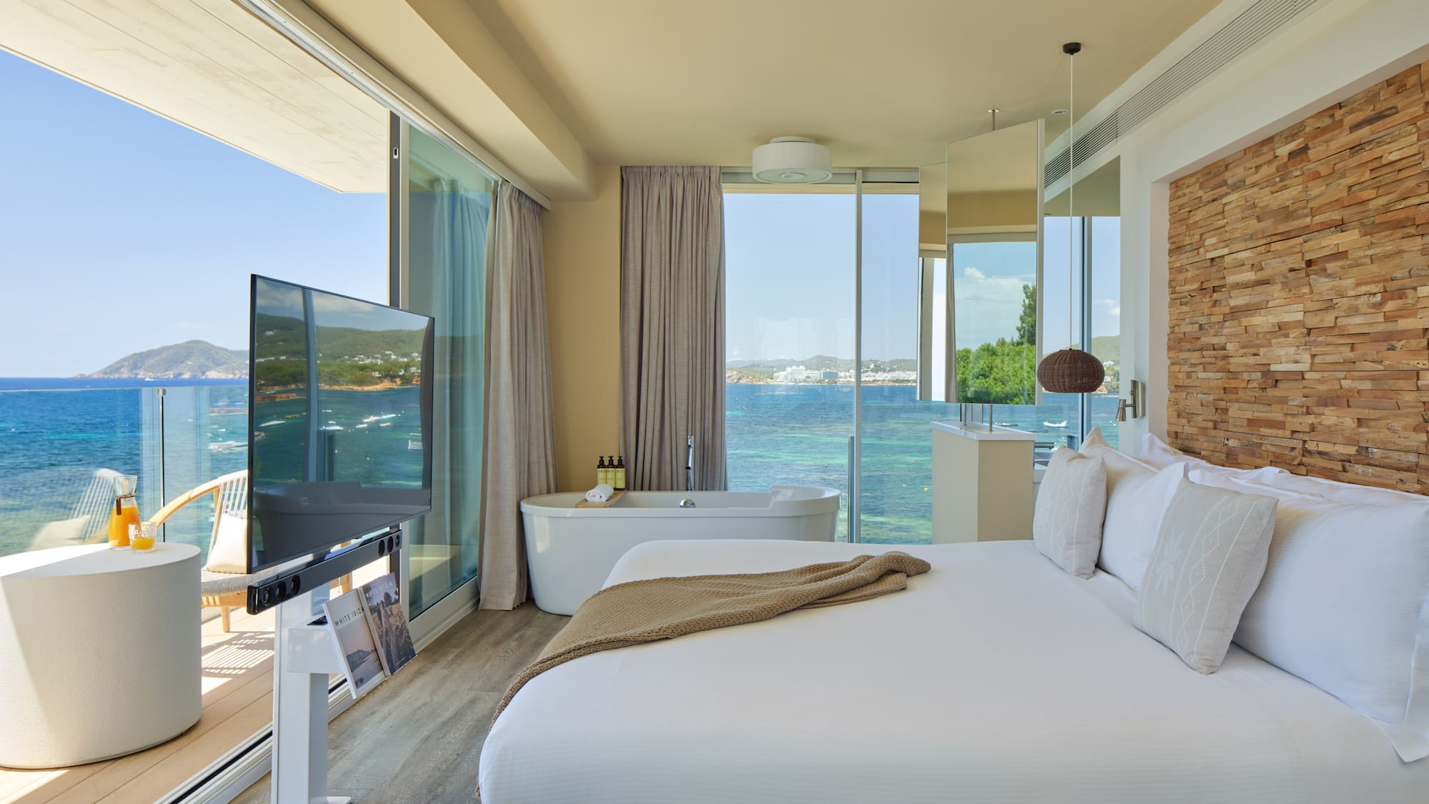 Luxury ocean view hotel suite with bed, freestanding tub, and balcony.