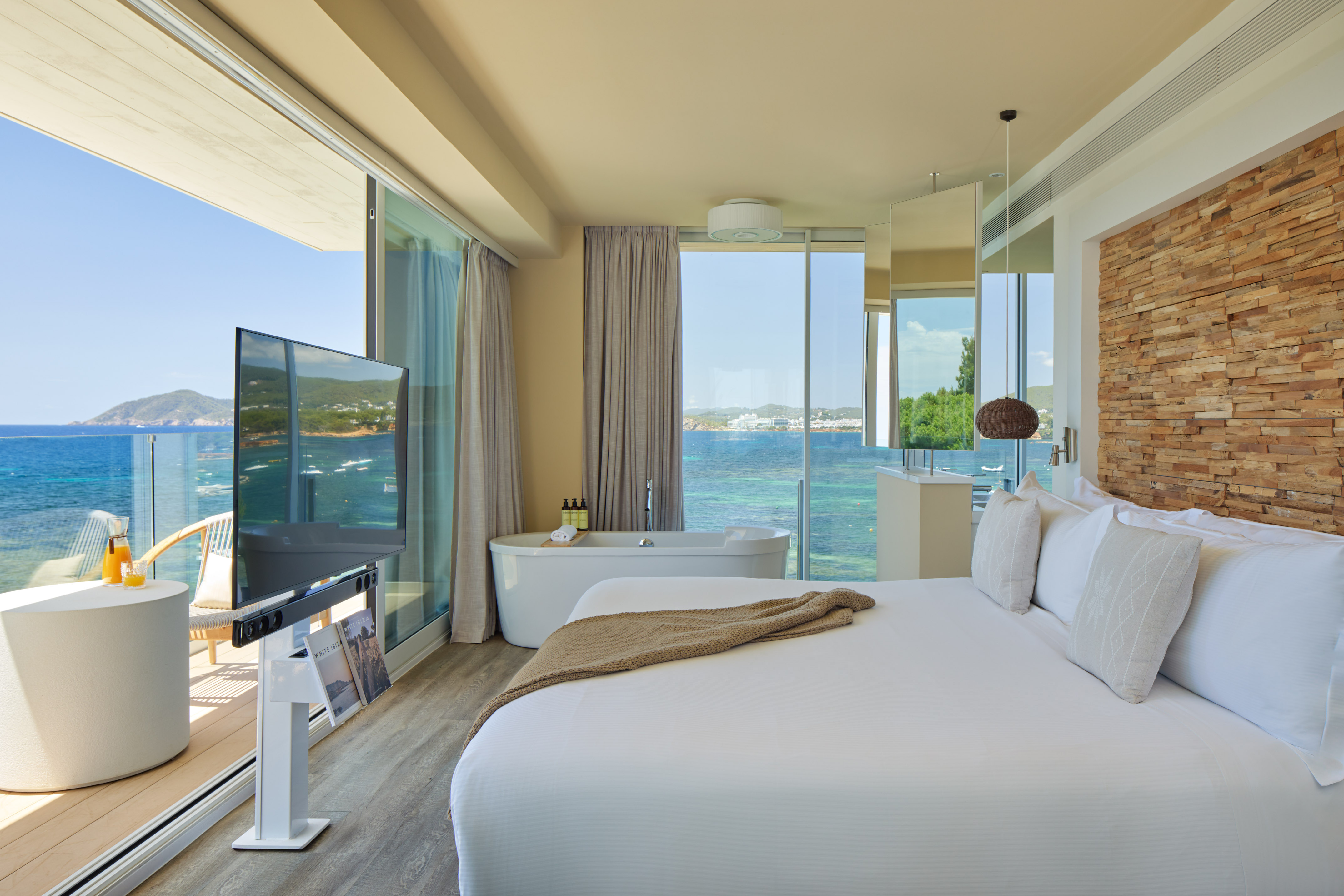 Luxury ocean view hotel suite with bed, freestanding tub, and balcony.