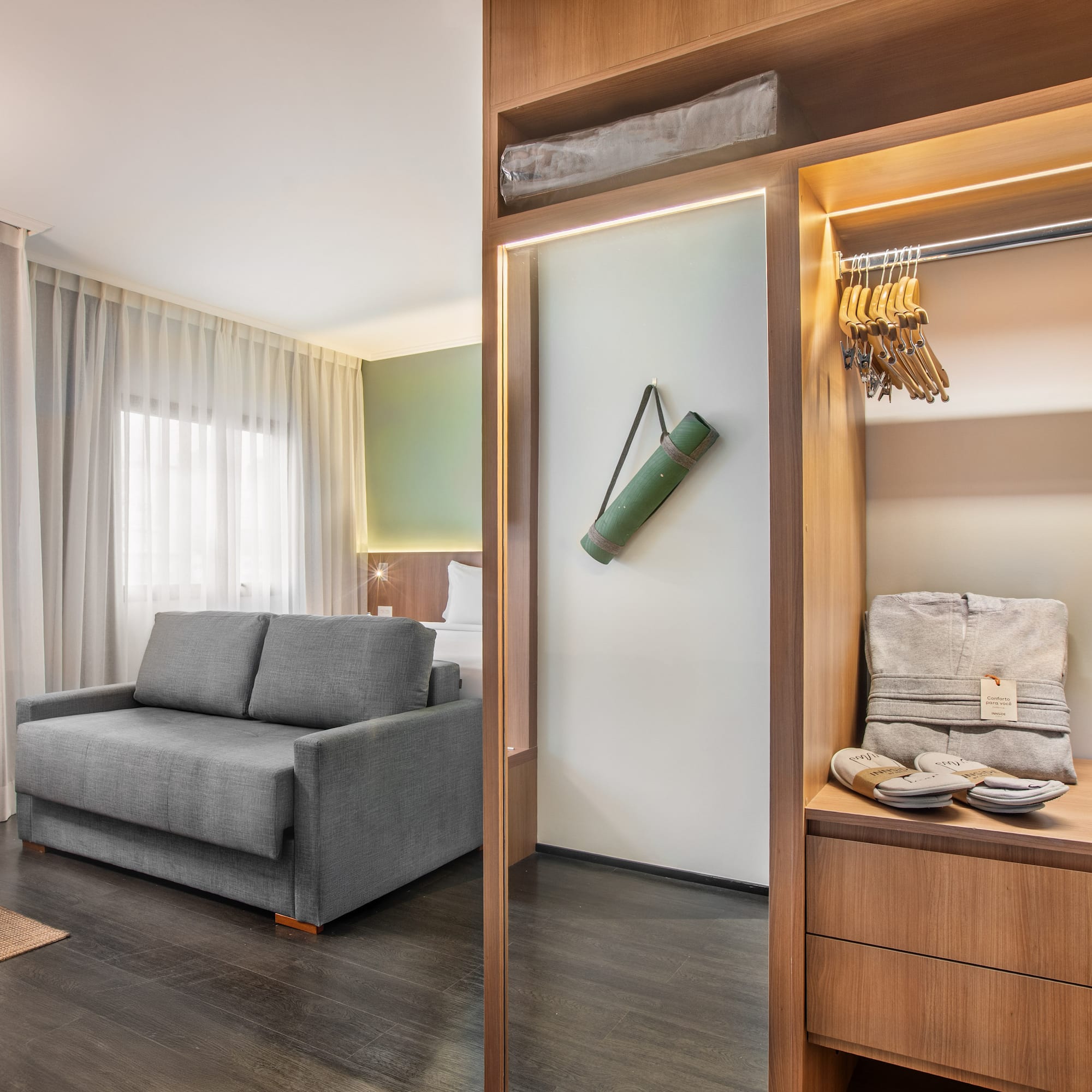 Habitación de hotel con sofá cama, armario con plancha y esterilla de yoga.