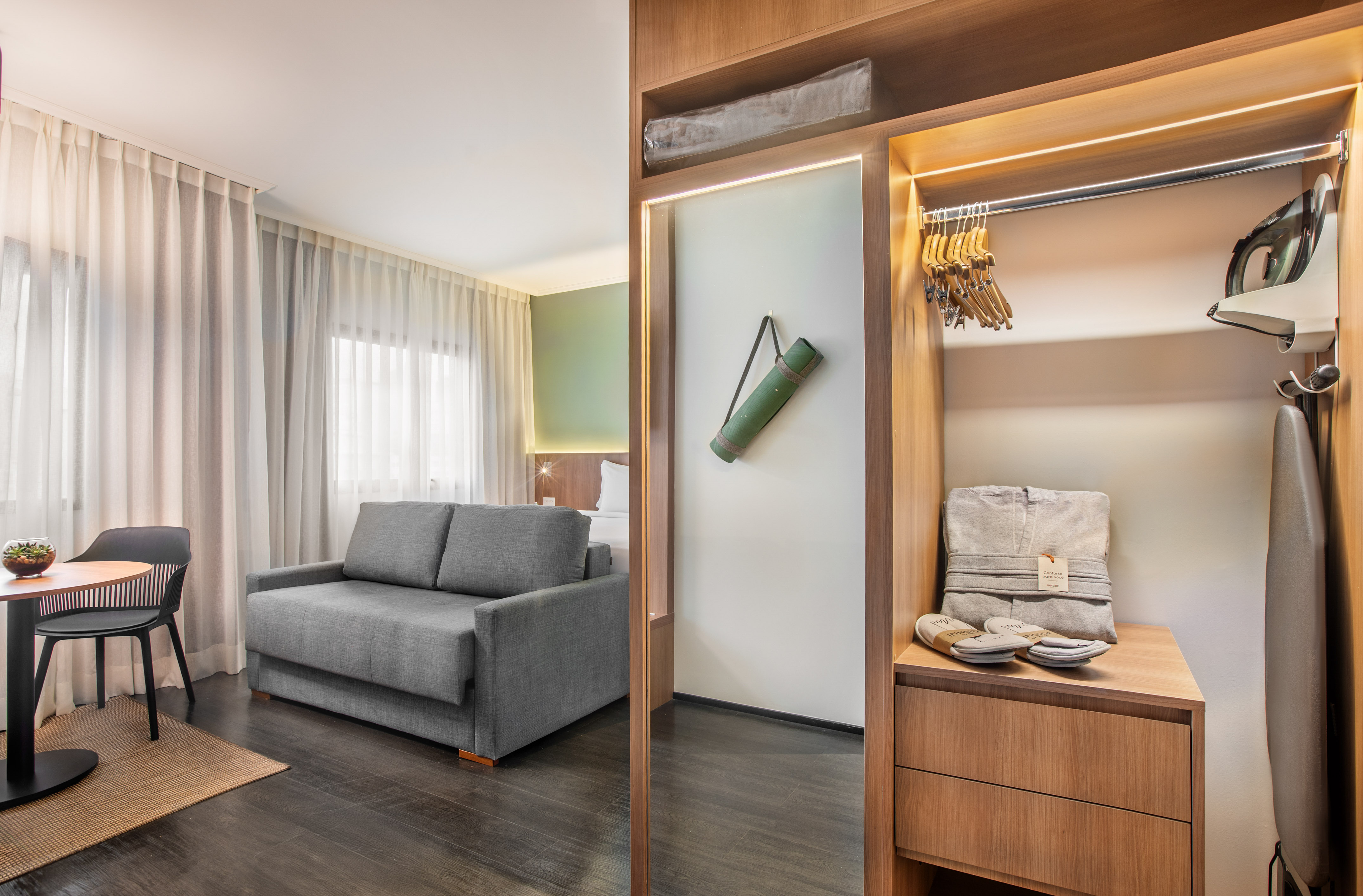 Habitación de hotel con sofá cama, armario con plancha y esterilla de yoga.