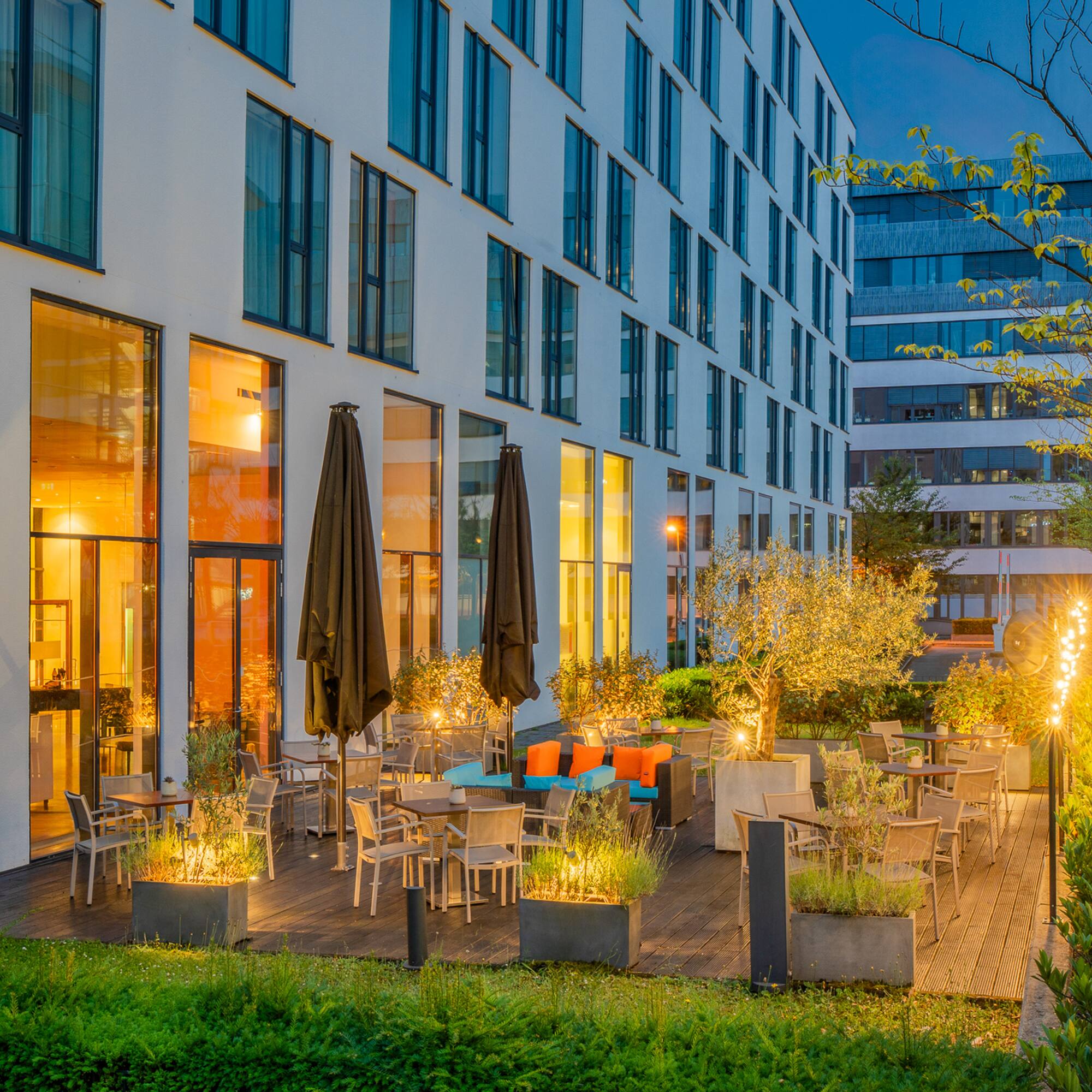 Modern hotel patio with outdoor seating, illuminated by warm evening lights.