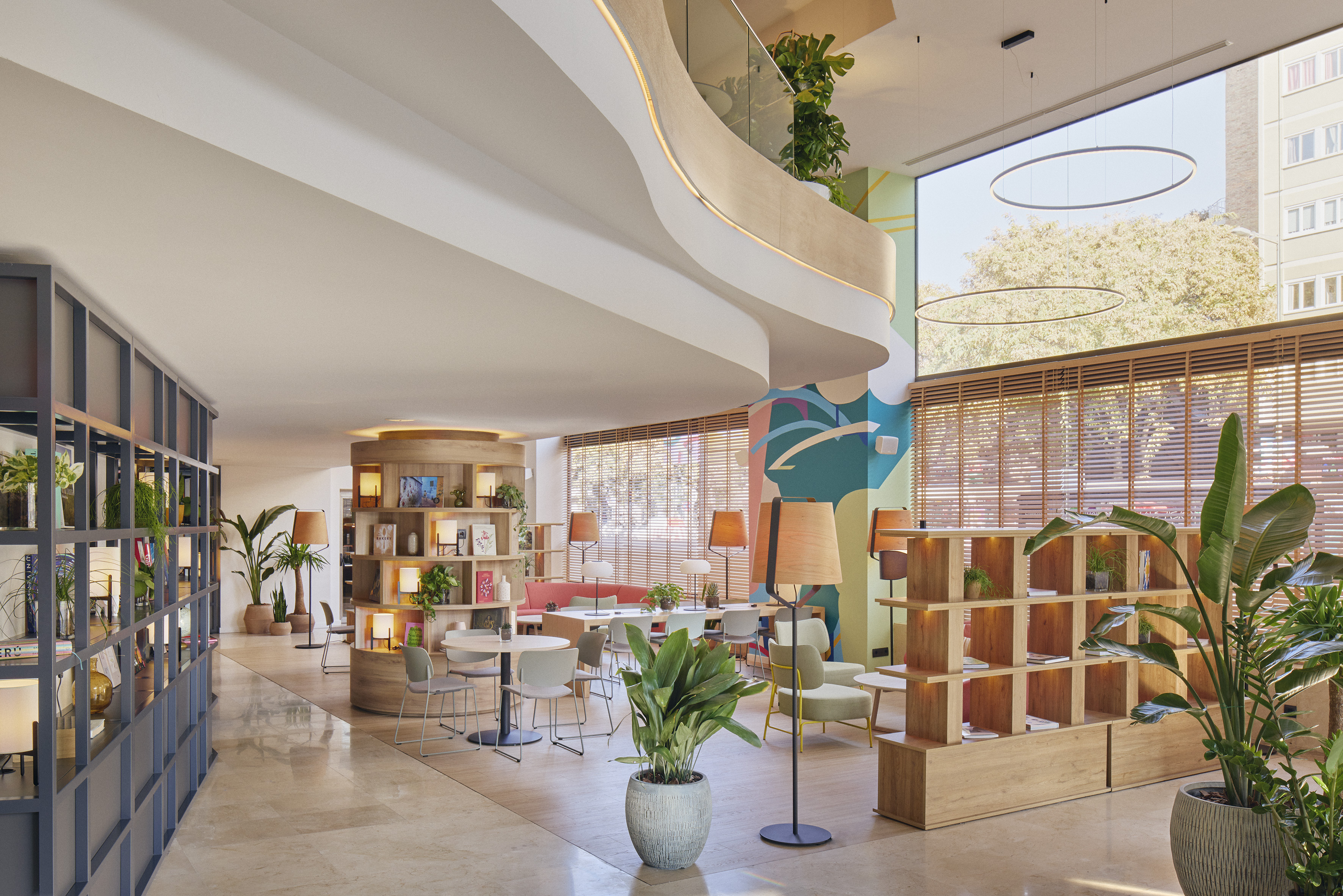 Modern hotel lounge with curved mezzanine, round bookshelves, and natural light.