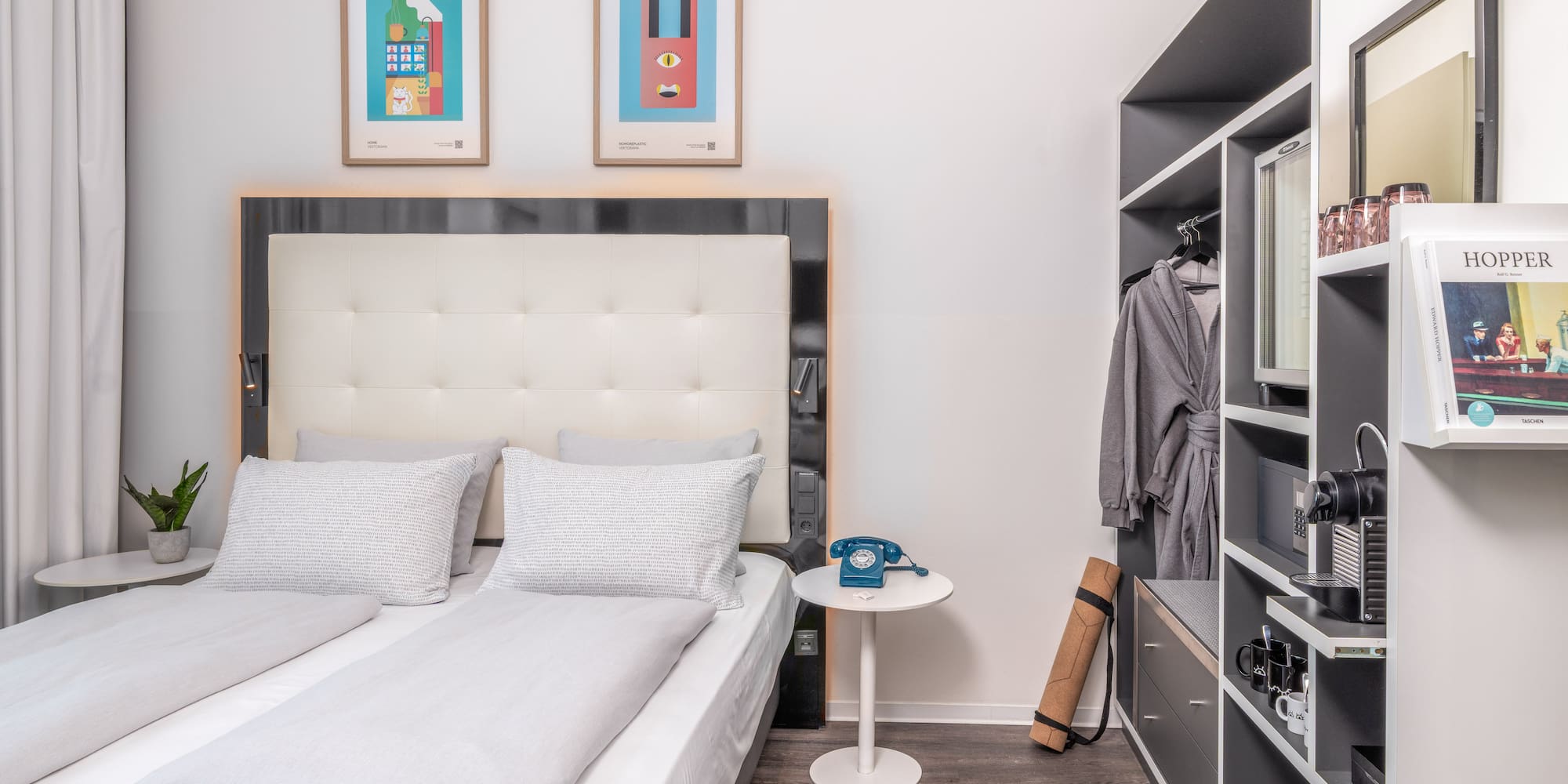 Modern hotel bedroom with light grey bed, colorful art, and built-in closet.