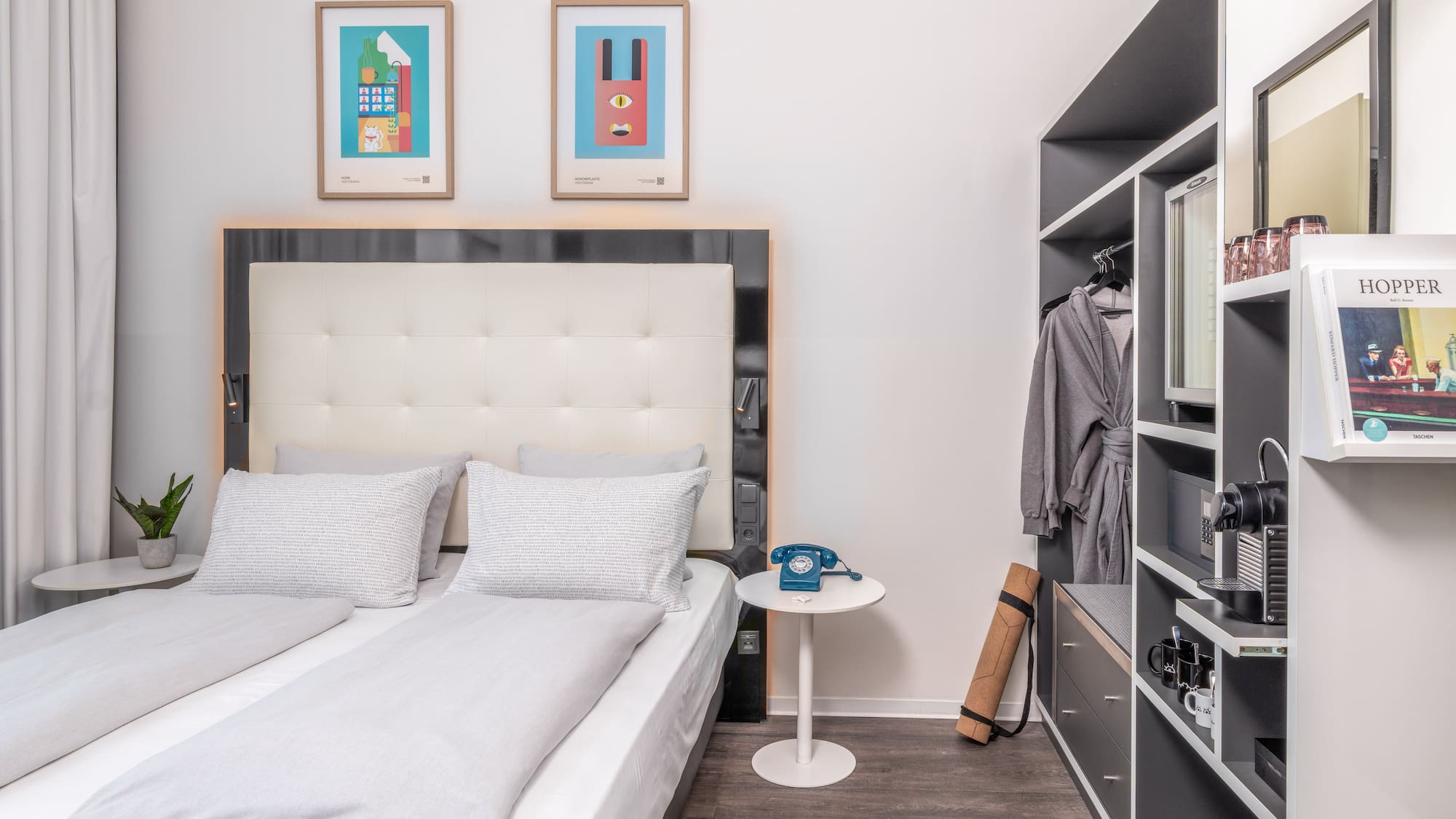 Modern hotel bedroom with light grey bed, colorful art, and built-in closet.