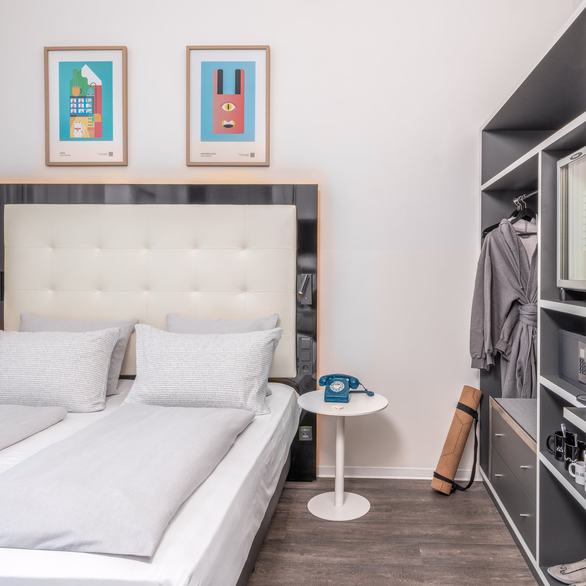 Modern hotel bedroom with light grey bed, colorful art, and built-in closet.